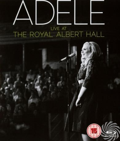 Adele op het podium, zingt in een microfoon, met de tekst 'ADELE'.