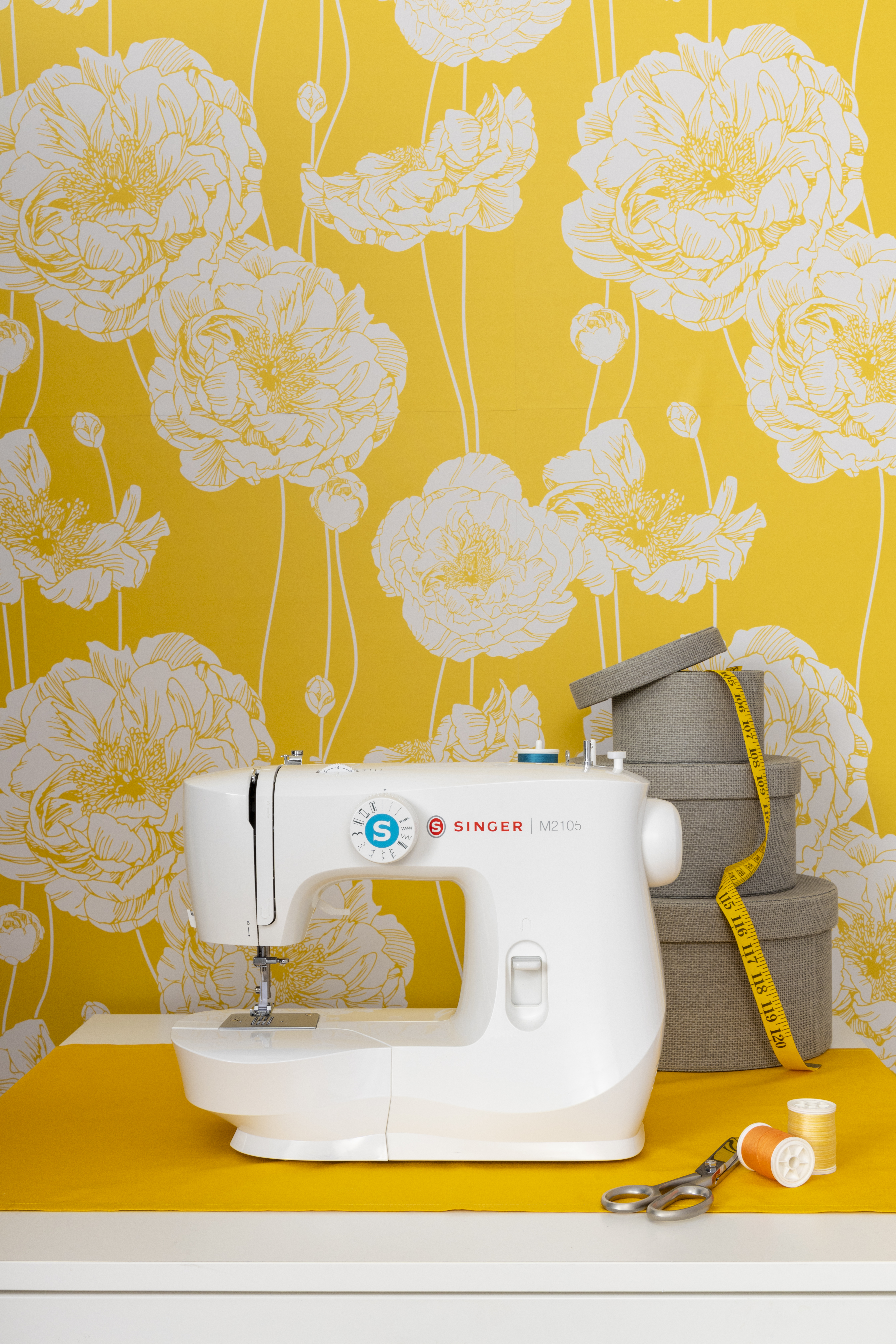A white sewing machine on a yellow surface with floral wallpaper.