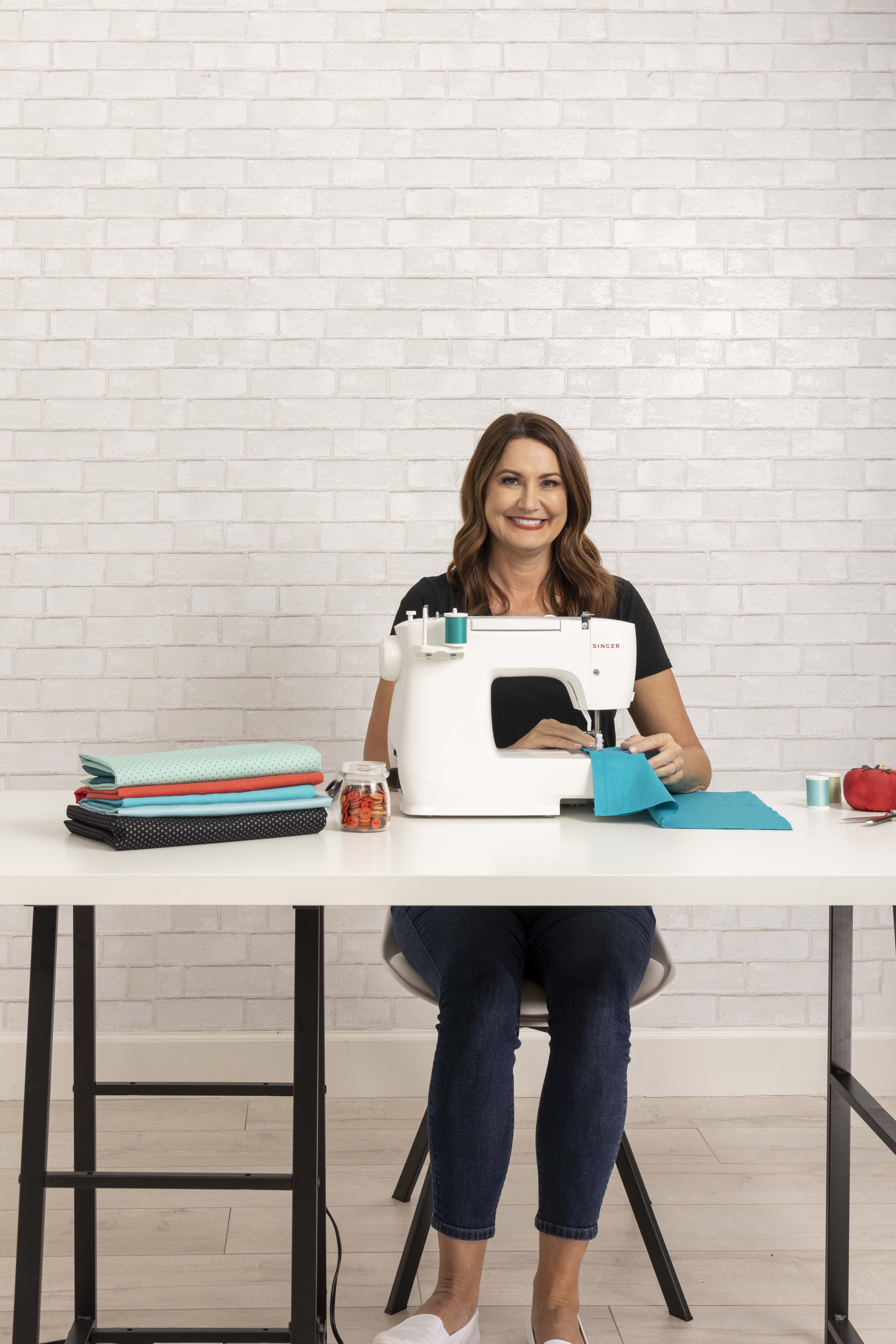 Woman sewing with a white Singer sewing machine, on a white desk.