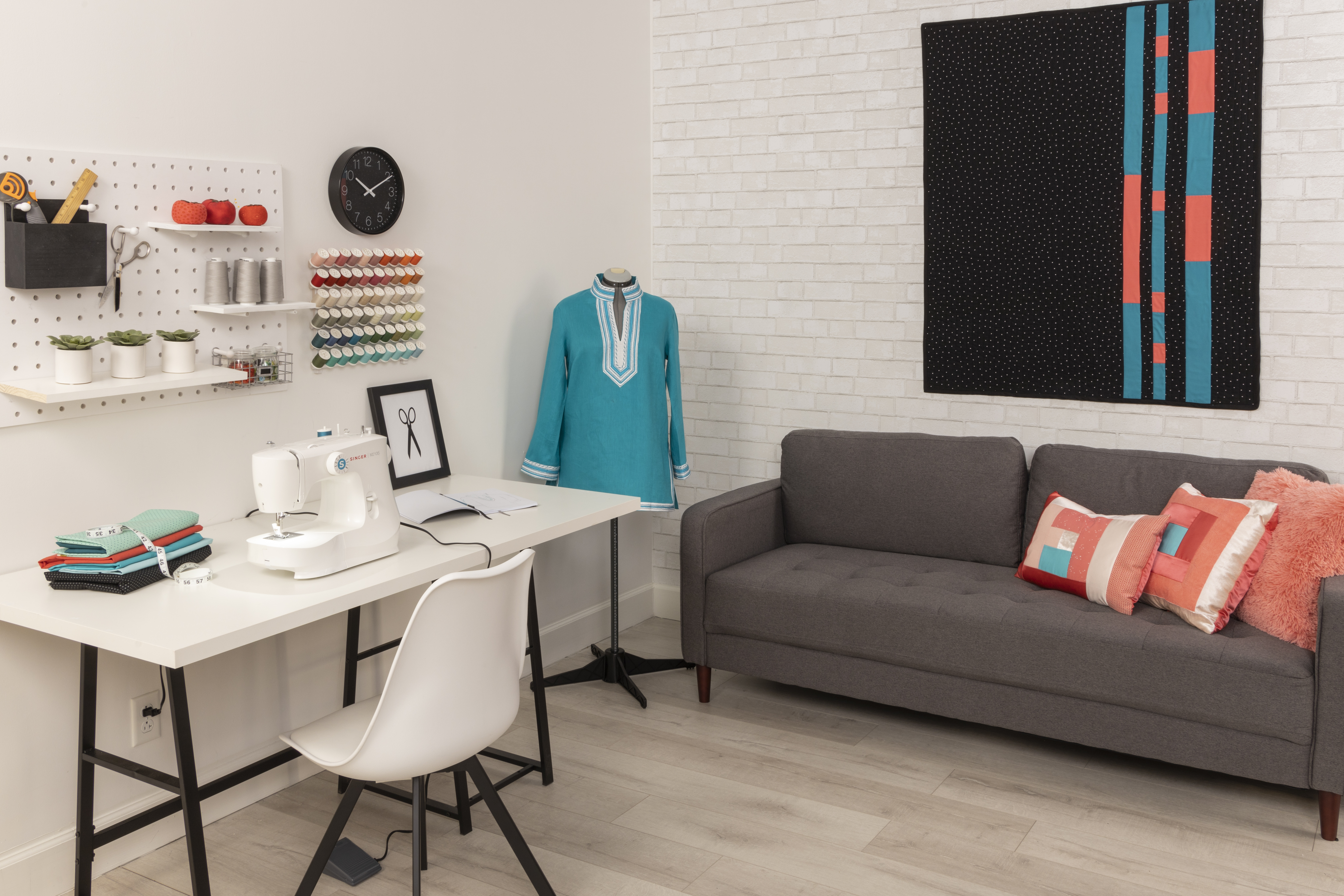 A sewing room with a sewing machine, supplies, and a mannequin wearing a teal tunic.