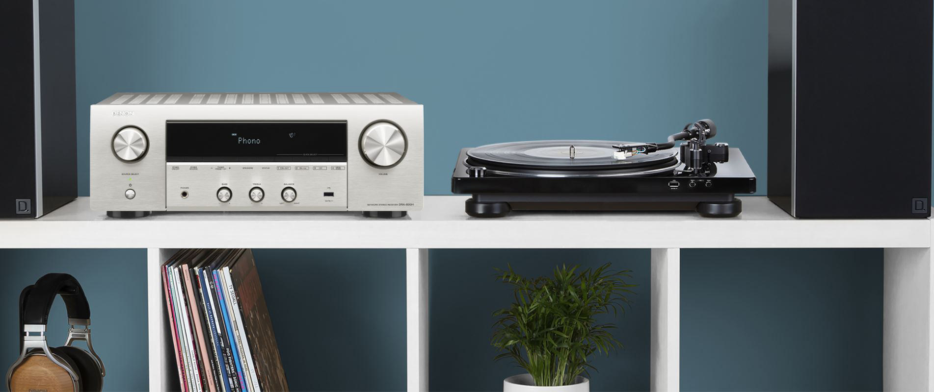 Ein Heim-Audio-Setup. Ein silberner Receiver, ein Plattenspieler, schwarze Lautsprecher, Regal mit Schallplatten.