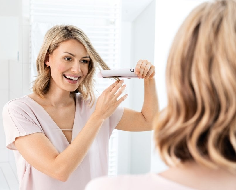 Une femme se coiffant devant un miroir avec un lisseur.