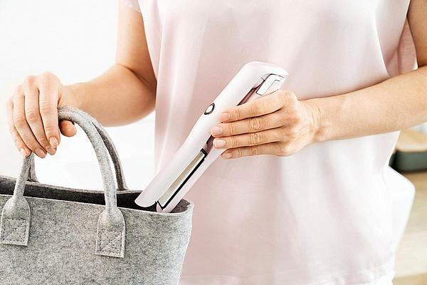 Une personne tient un lisseur rose et un sac gris.