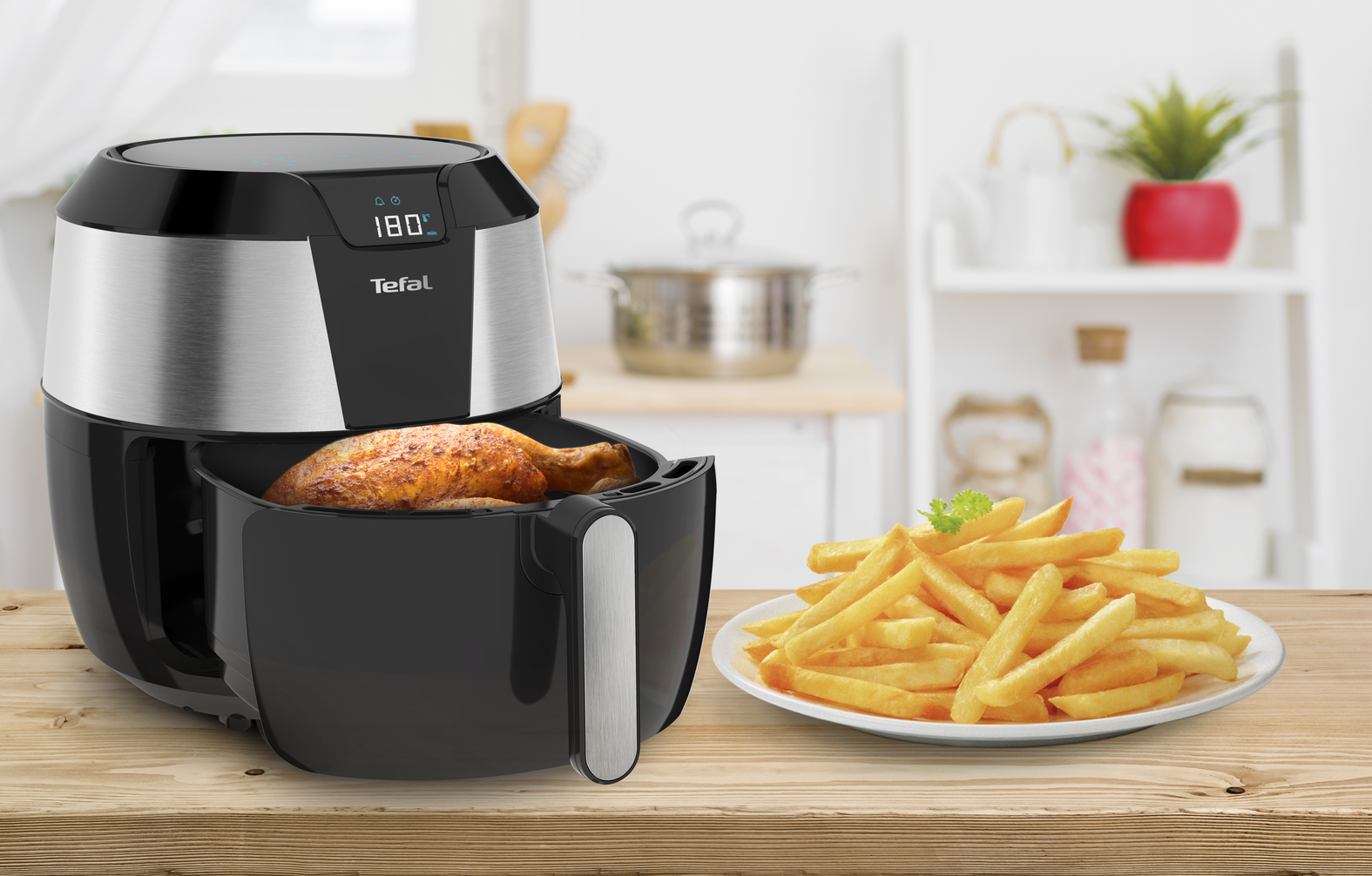 An air fryer with fried chicken and french fries on a wooden table.