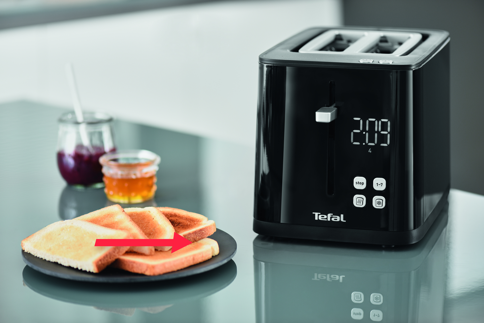 Een zwarte Tefal-broodrooster met toast en jam op een bord, een pijl wijst van de toast naar de broodrooster.