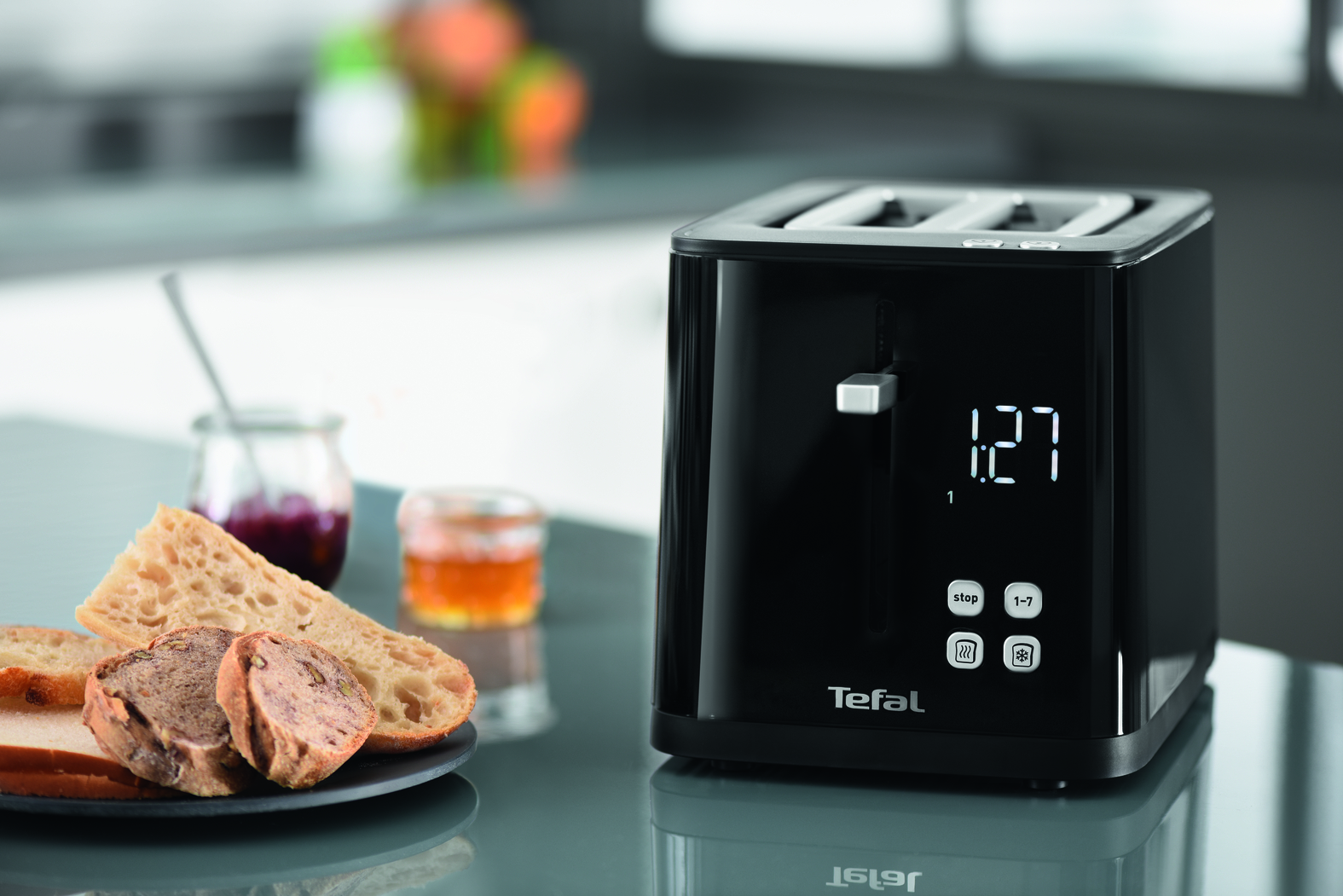 Zwarte broodrooster met brood, jam en honing. Tefal-merk en tijdweergave zichtbaar.