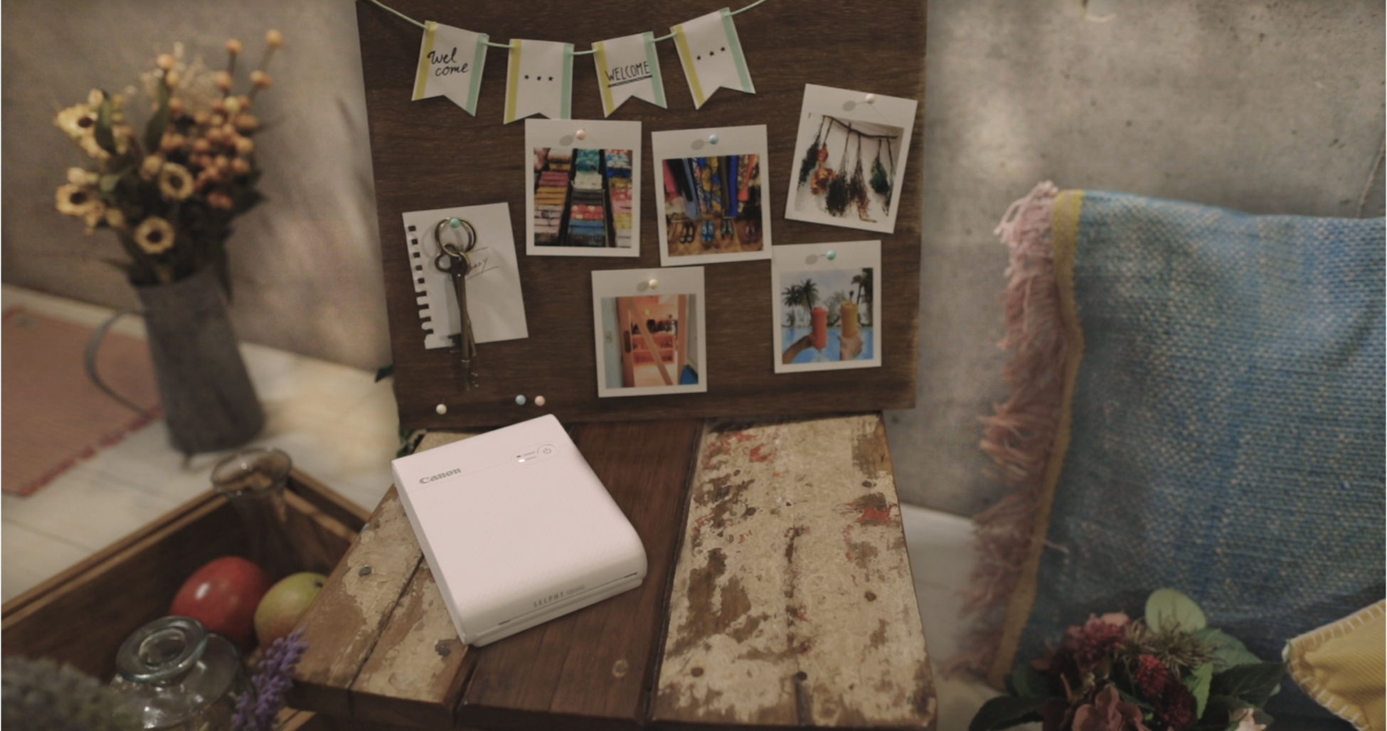 Canon Selphy Square printer, photos on wooden board with decorations. Flowers and pillows.