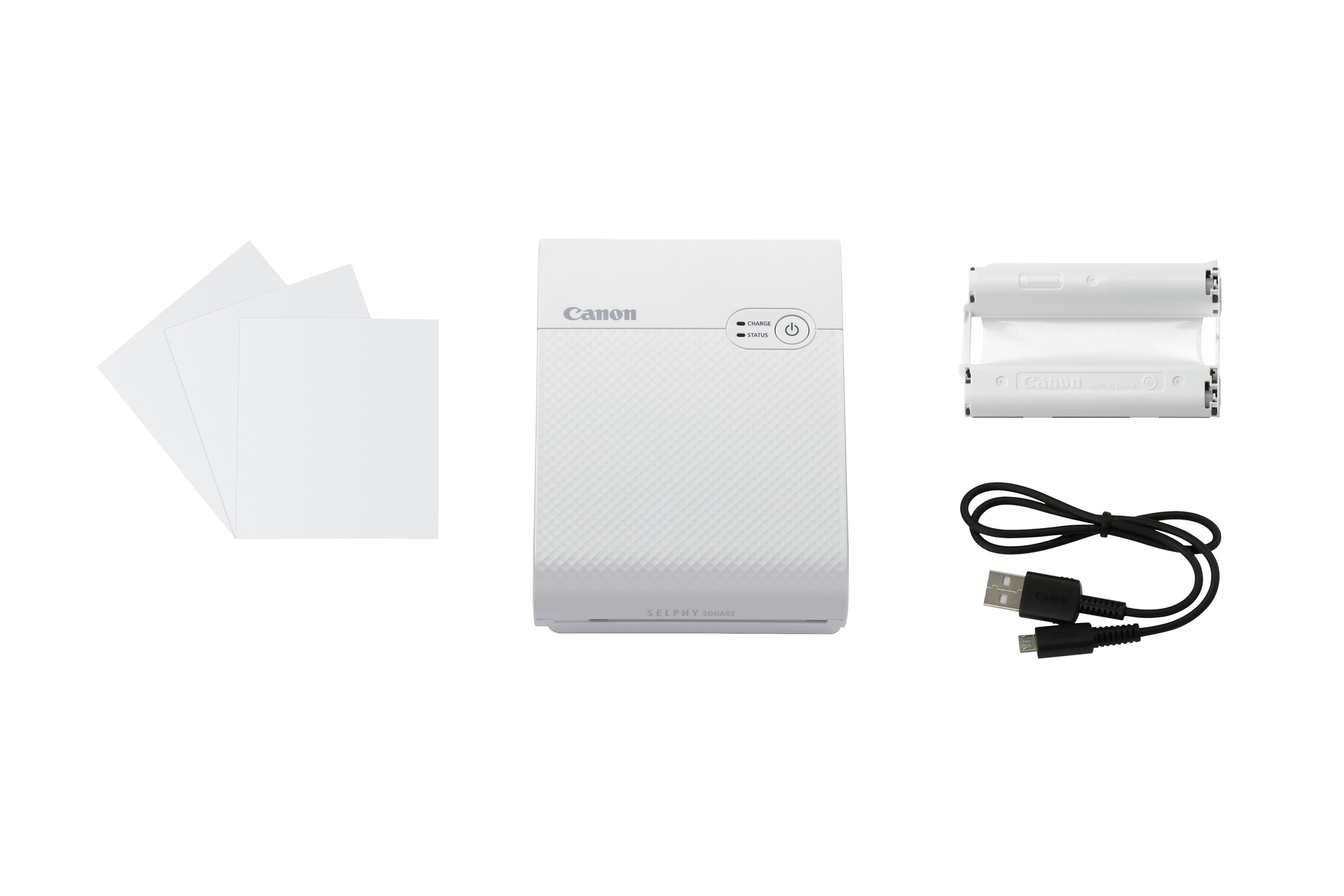 A white Canon Selphy printer with photo paper, batteries, and a USB cable.
