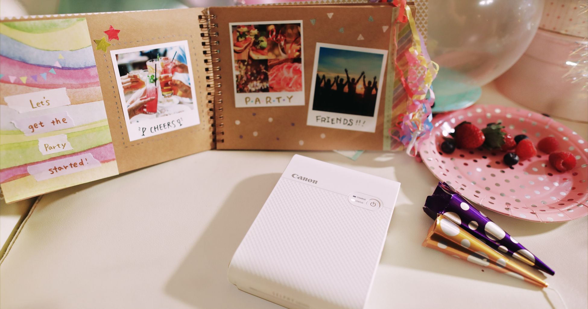 Canon Selphy Square printer and an open album with photos and decorations. Party theme.