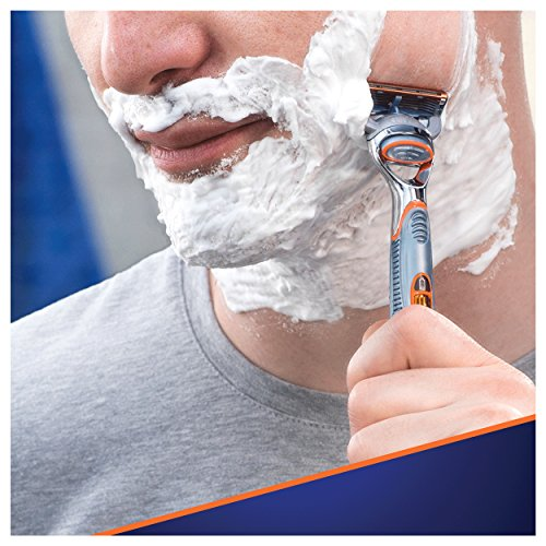 Un hombre afeitándose. Tiene crema de afeitar en la cara y está usando una maquinilla.