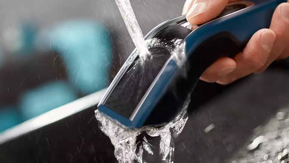 L'eau coule sur un rasoir électrique noir et bleu, tenu par une main.