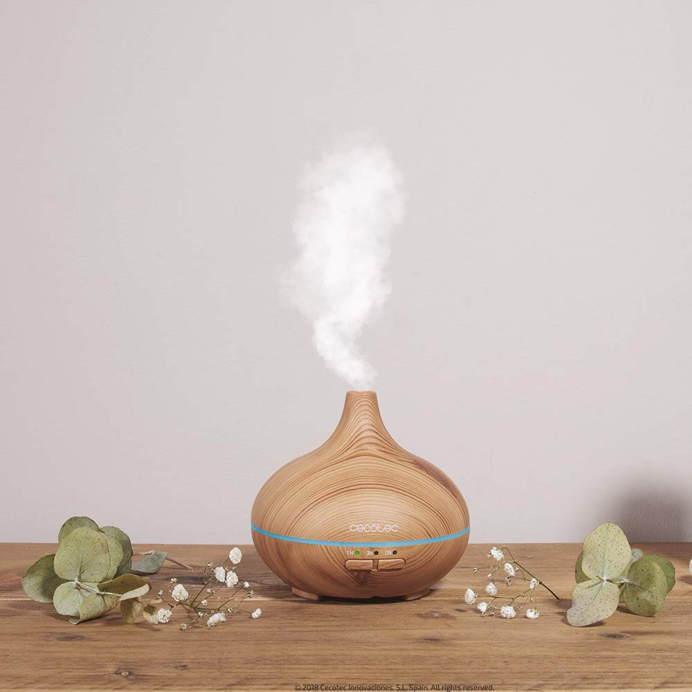 Difusor de aromaterapia de madera con vapor, junto a plantas en mesa de madera.