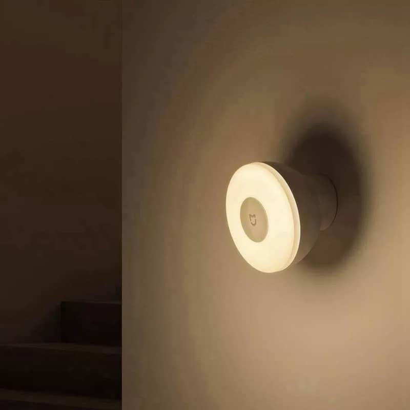 Una luz nocturna blanca circular montada en la pared con un logotipo, brillando en una habitación tenue.