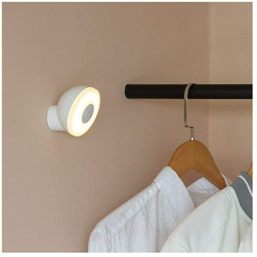 Una lámpara blanca y redonda está montada en una pared junto a una barra de armario con ropa.