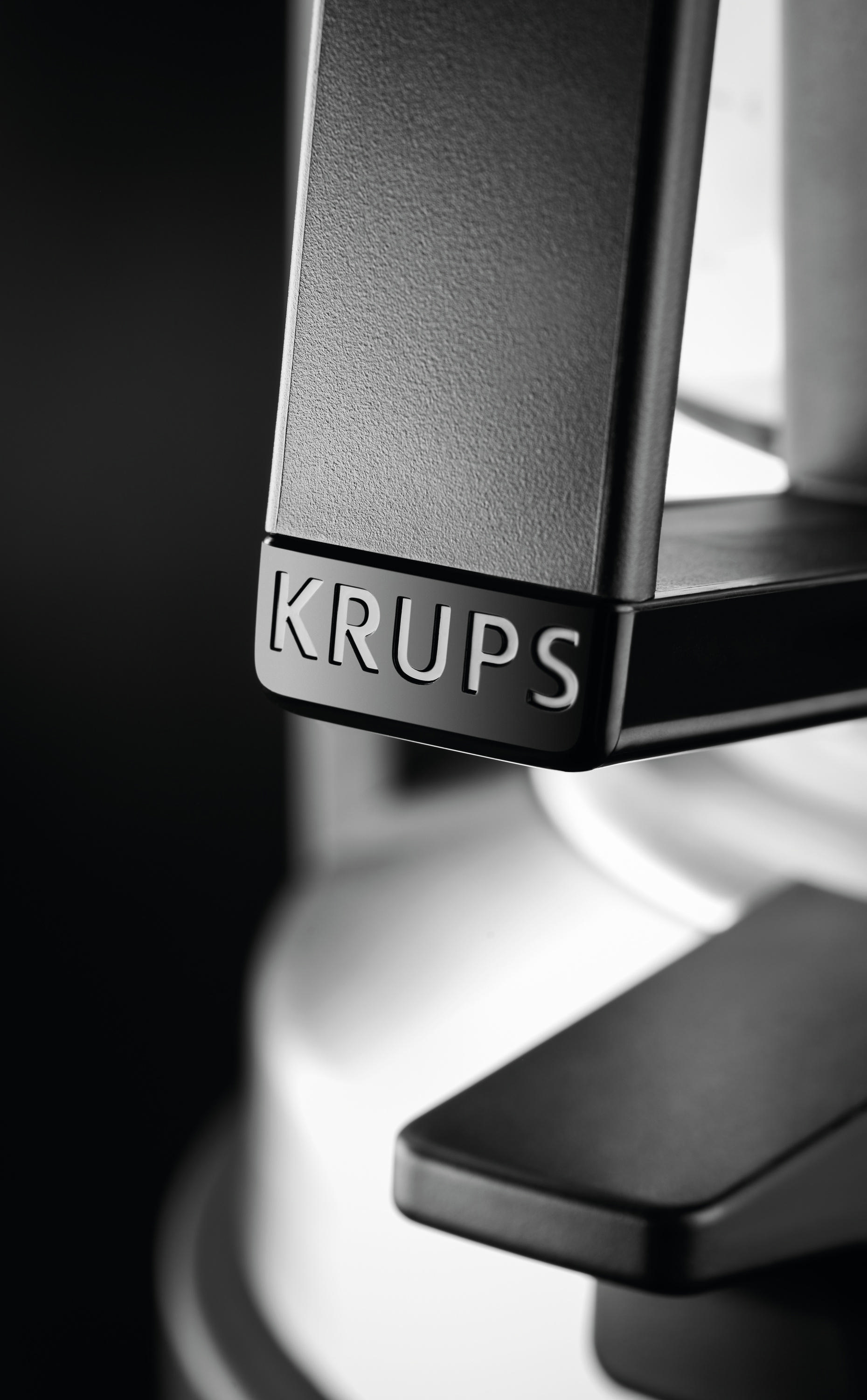Nahaufnahme einer schwarzen Krups Kaffeemaschinenkomponente. Der Markenname ist sichtbar. Schwarzer Hintergrund.