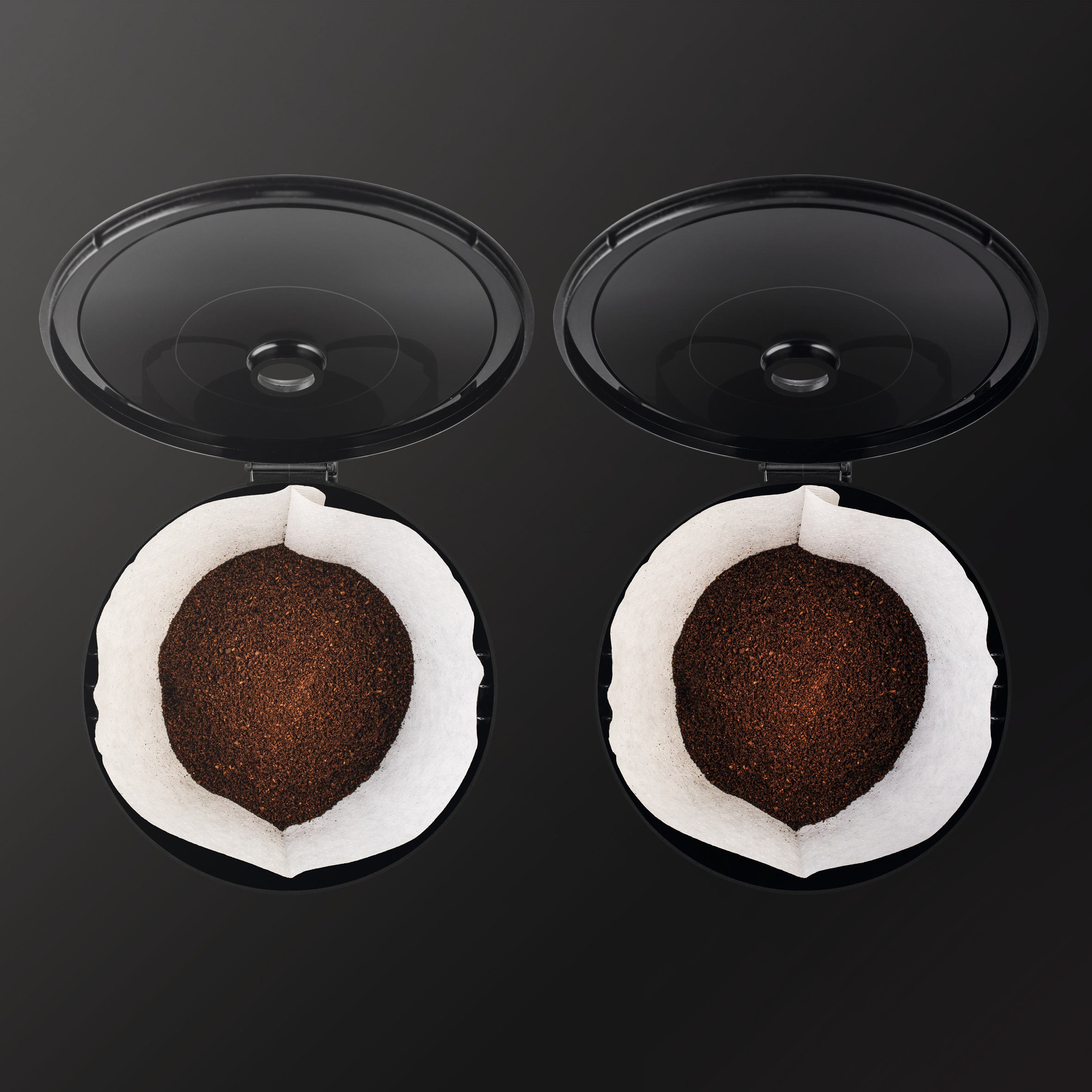 Zwei offene schwarze Kaffeefilterhalter mit Kaffeepulver darin.