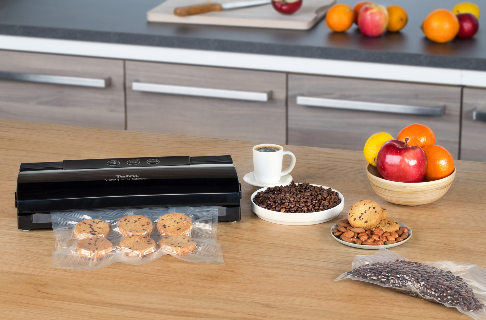 Keuken met een vacuüm sealer, koffie, koekjes en fruit op een houten tafel.