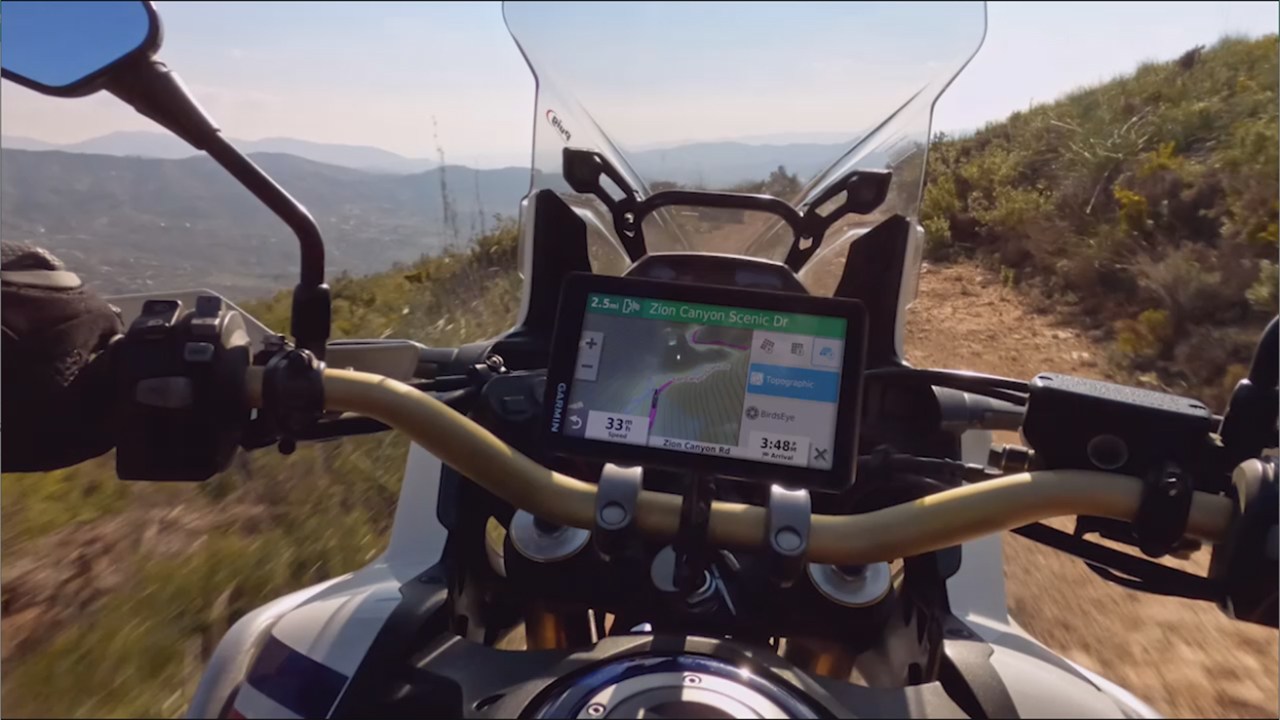 Vista del cruscotto della moto. Mostra uno schermo di navigazione. Strada e cielo montuosi.