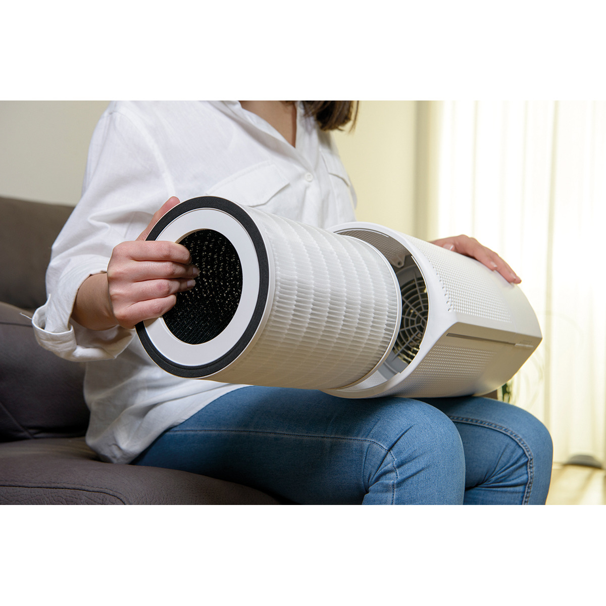 Una mujer sosteniendo un filtro de purificador de aire, sentada en un sofá.