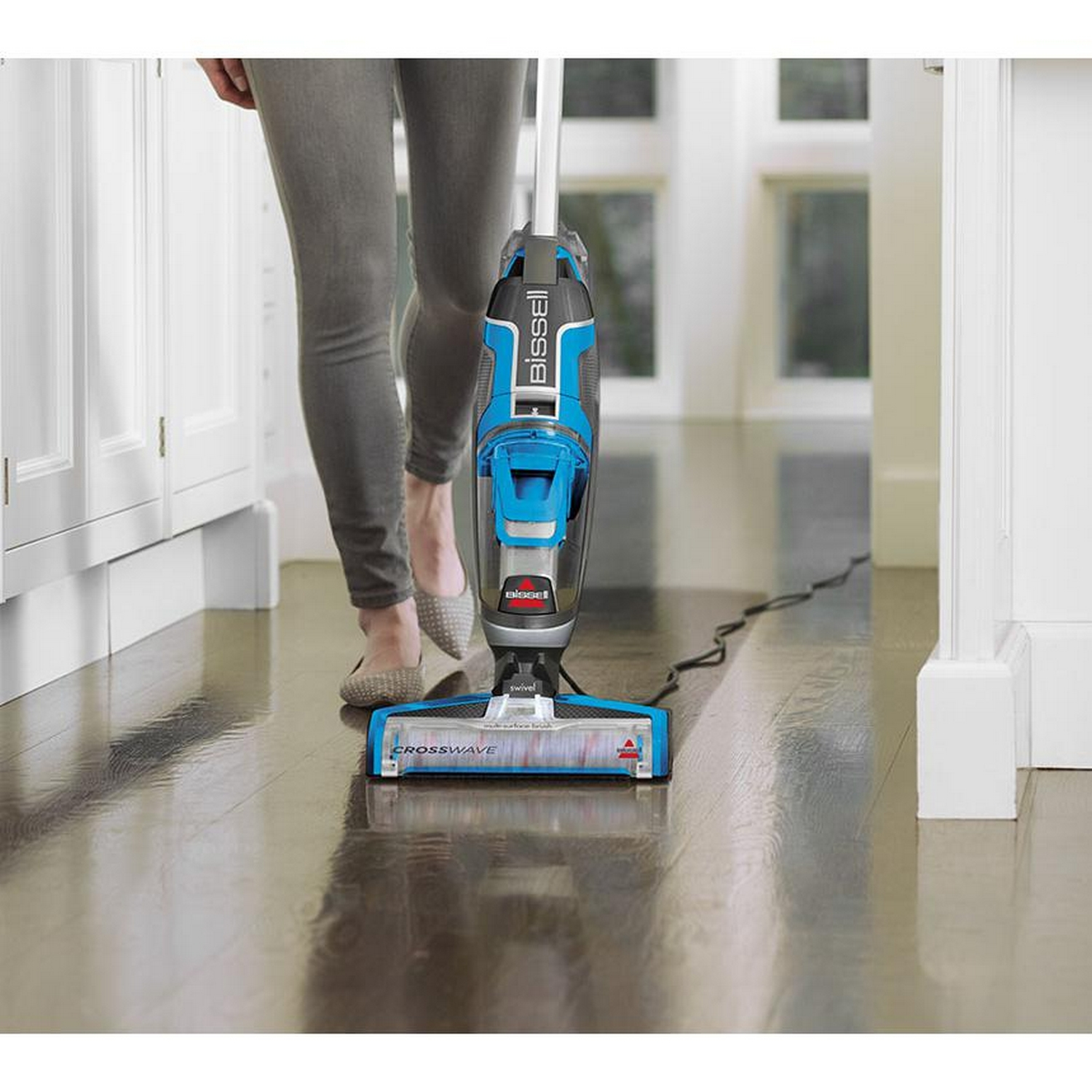 Una persona está limpiando un piso de madera con una limpiadora Bissell CrossWave azul y negra.
