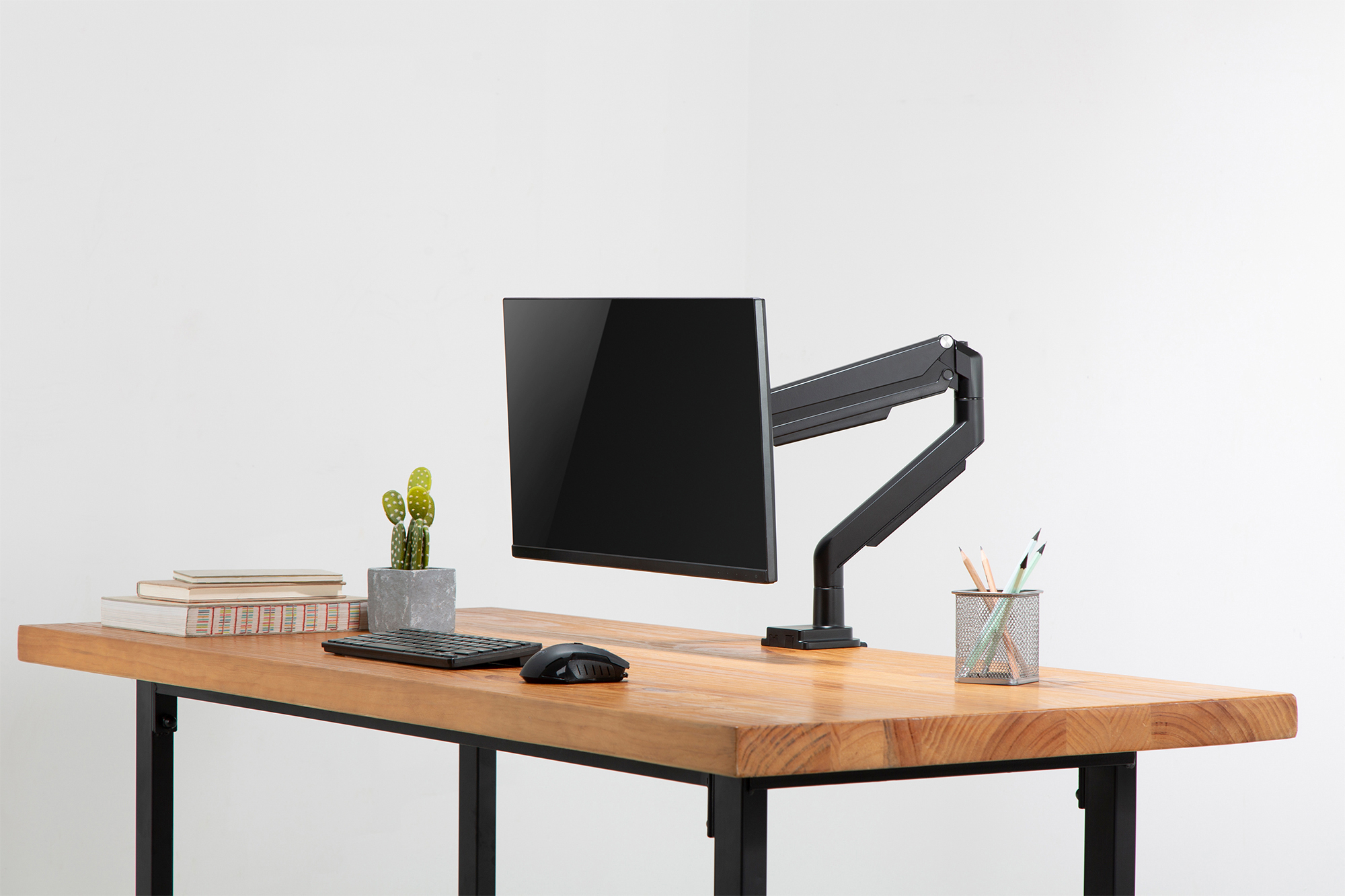 Schreibtisch mit Monitor an einem Arm, Tastatur, Maus, Kaktus und Bleistiften im Halter.