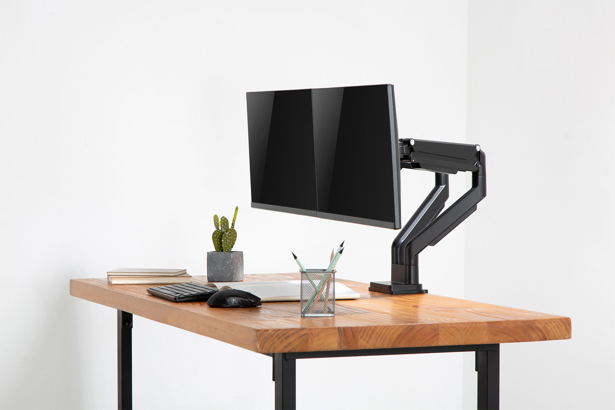 Monitor an einem schwarzen Armständer auf einem Holztisch, mit Kaktus, Tastatur und Stiften.