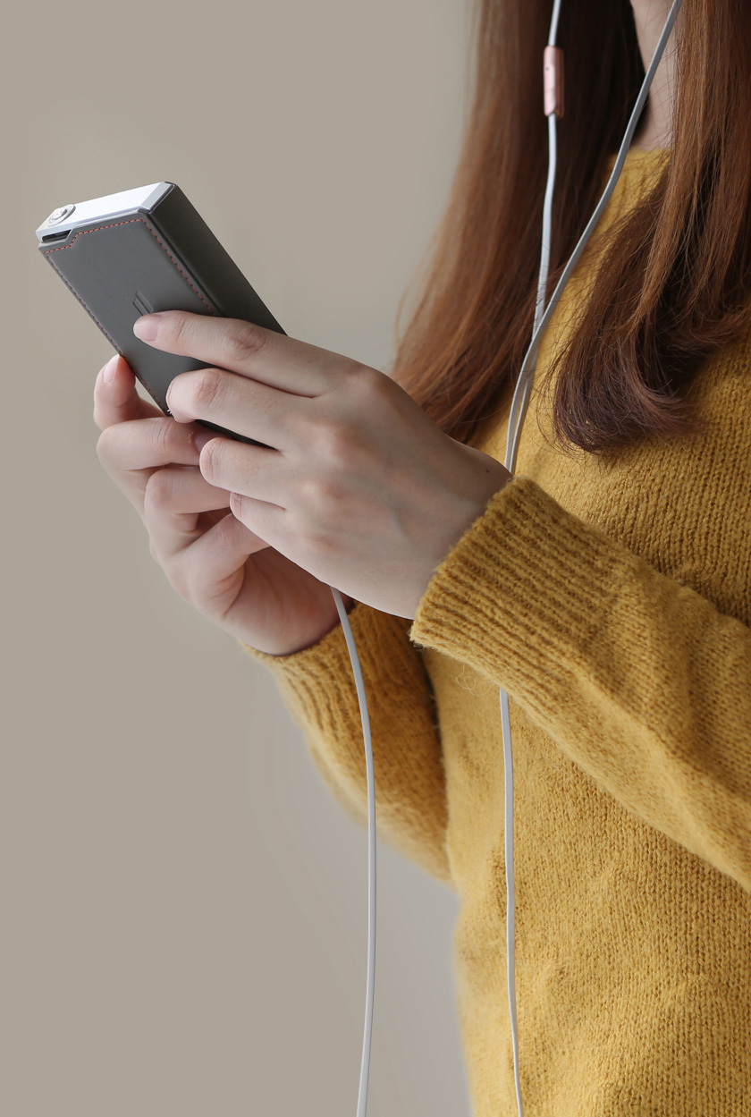 Une femme en pull jaune tient un téléphone avec des écouteurs blancs.