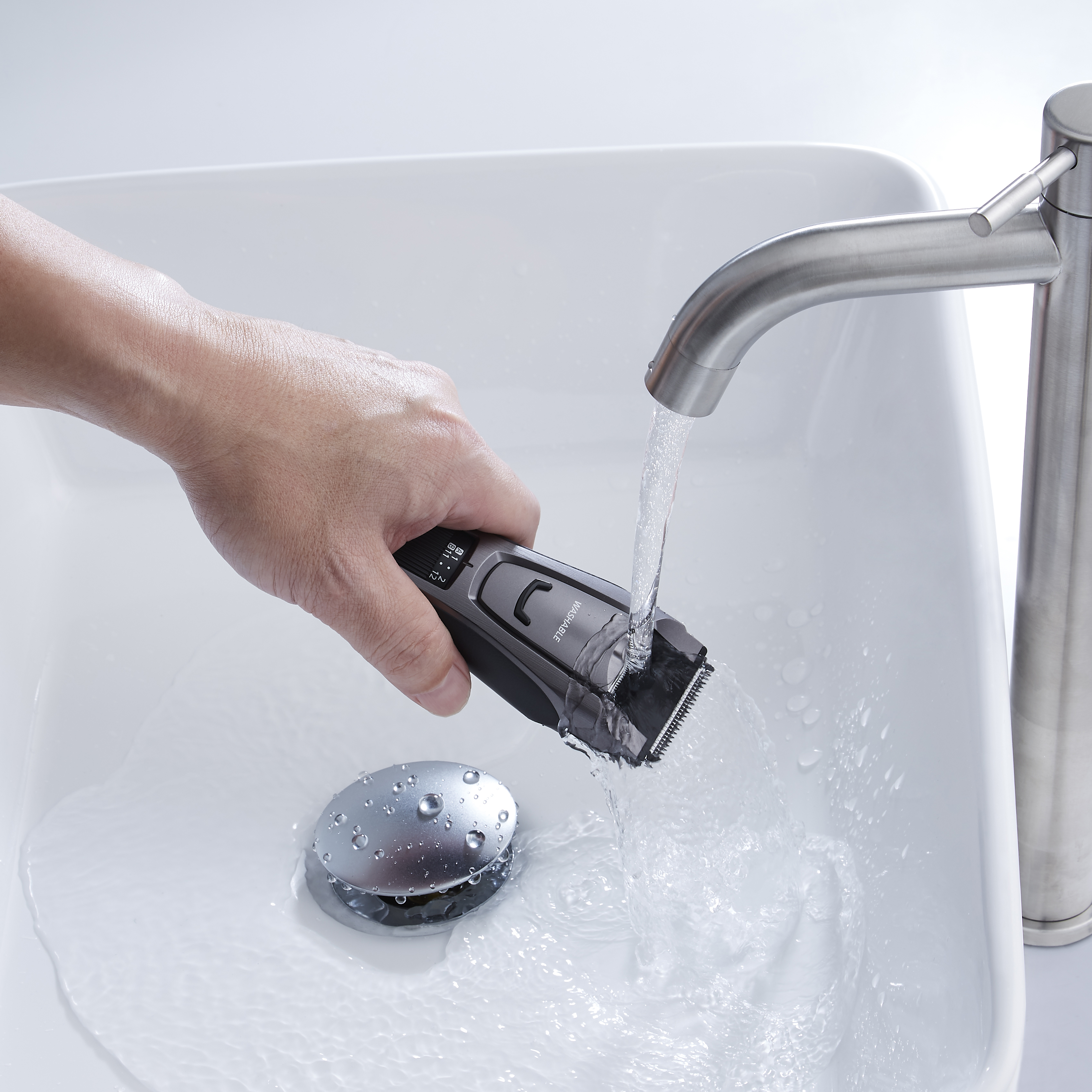 Die Hand einer Person spült einen schwarz-grauen Elektrorasierer in einem weißen Waschbecken ab.