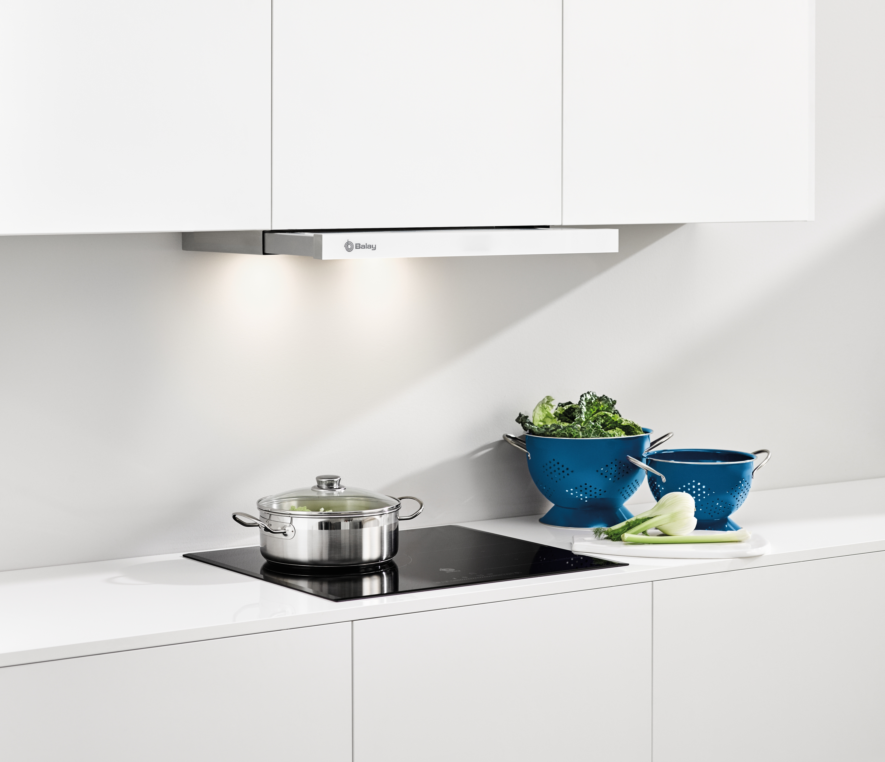 Escena de cocina con campana, vitrocerámica, ollas y coladores azules.