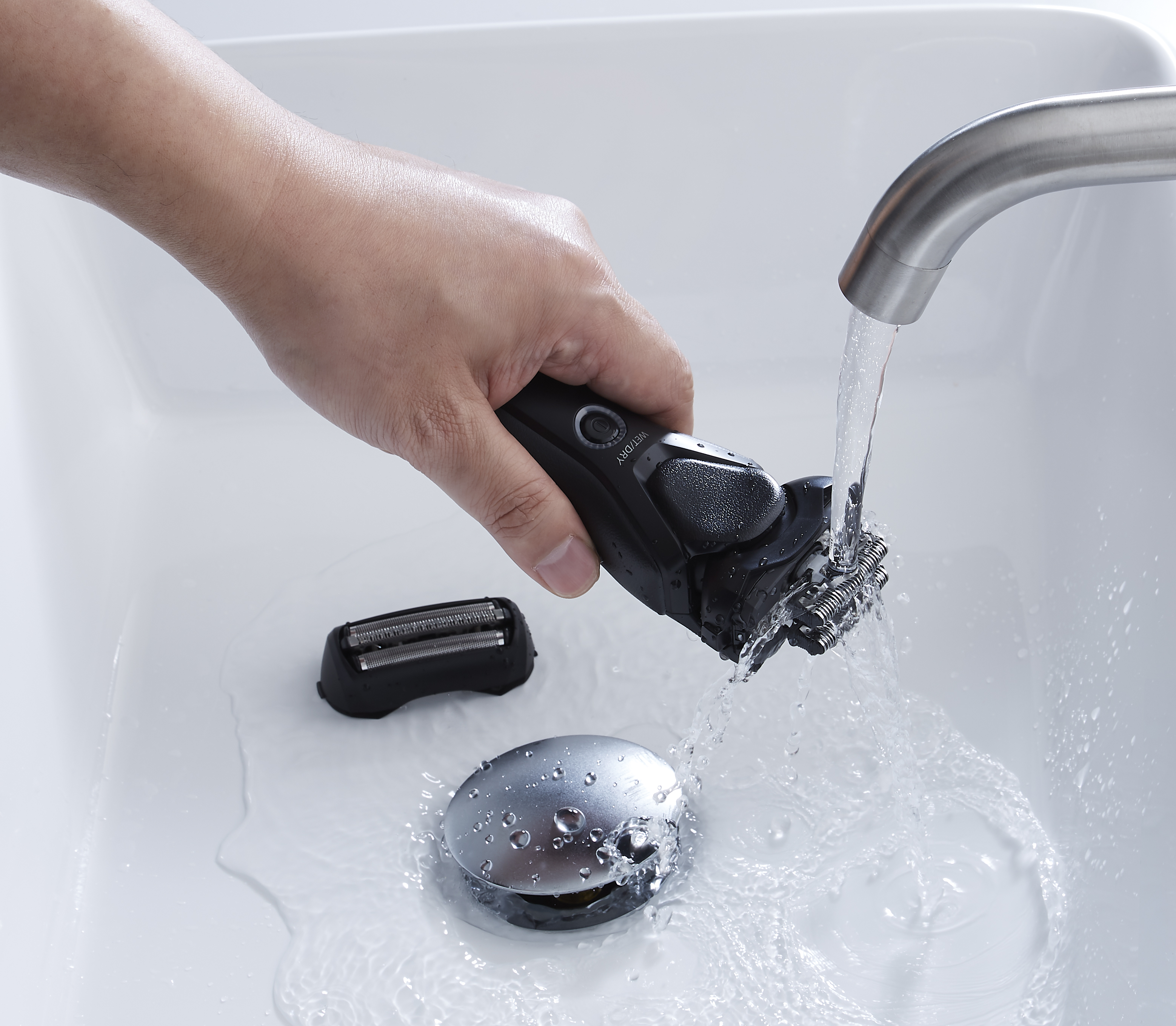 Ein schwarzer und grauer Rasierer wird in einem Waschbecken mit Wasser abgespült.