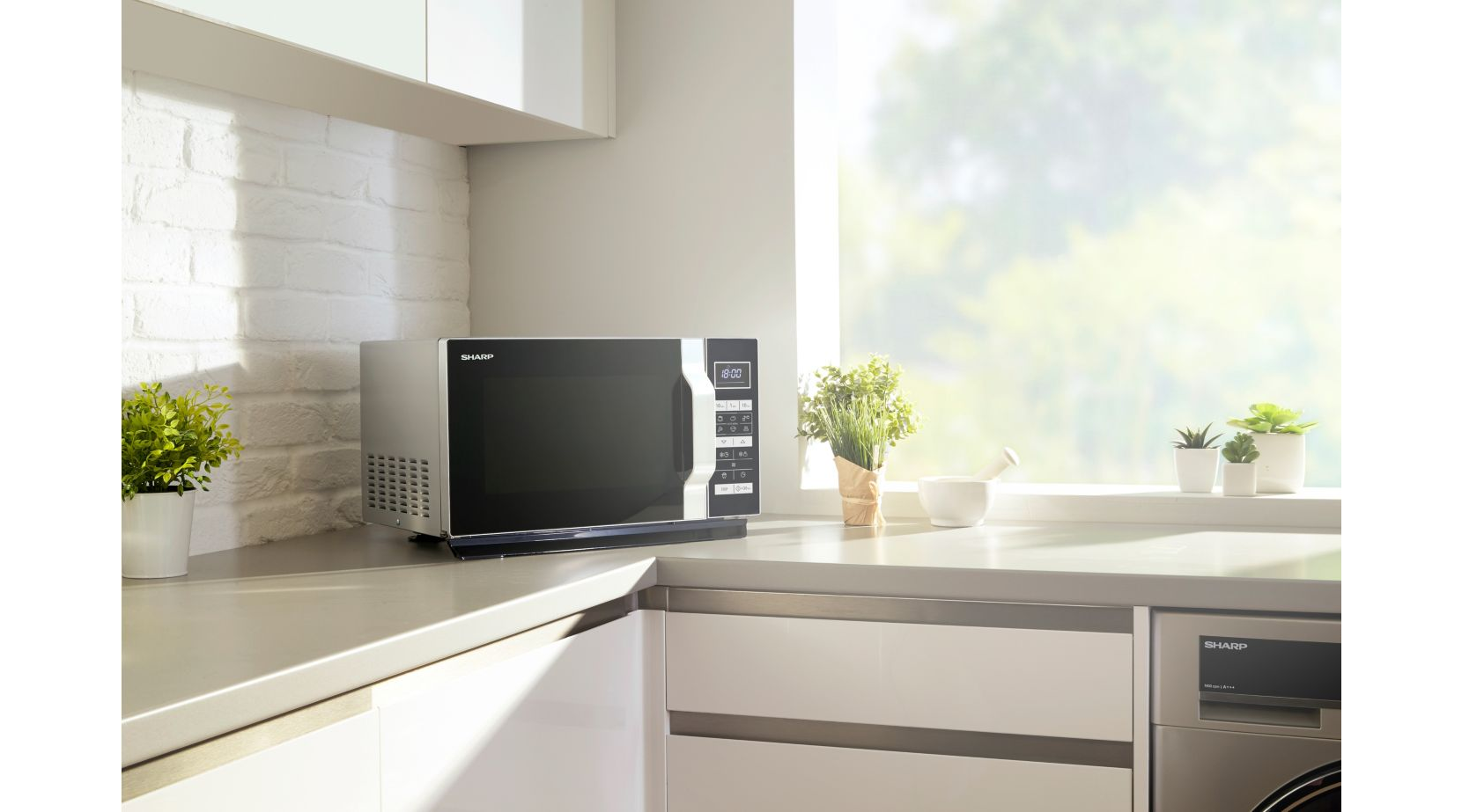Un micro-ondes sur un comptoir de cuisine. Autres éléments : plantes, fenêtre et mur en briques blanches.
