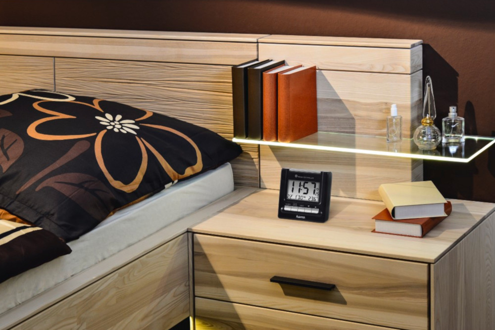 A bedroom scene with a bed, books, a clock, perfume bottles, and a nightstand.
