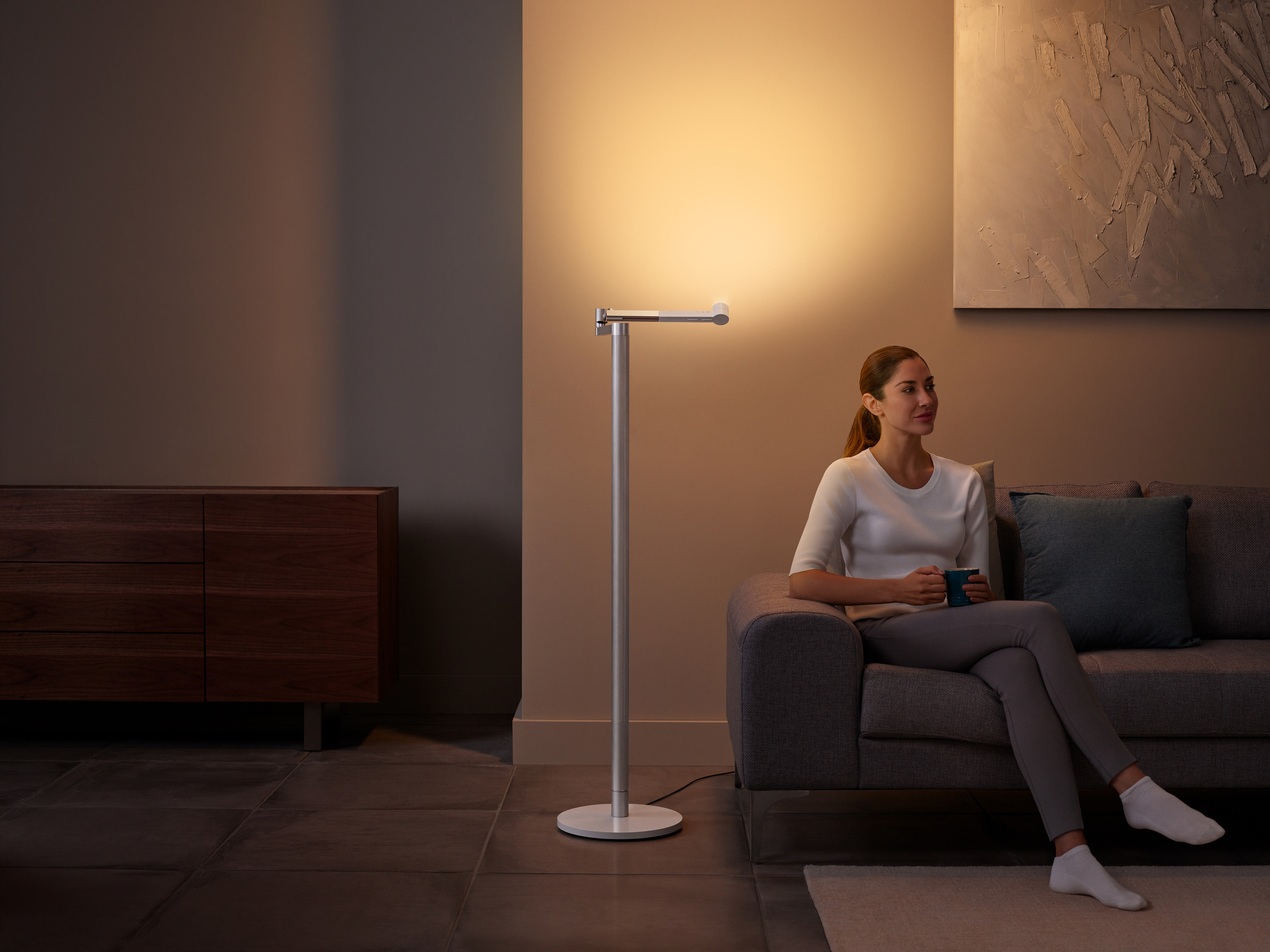 Eine Frau sitzt unter einer Stehlampe auf einem Sofa.