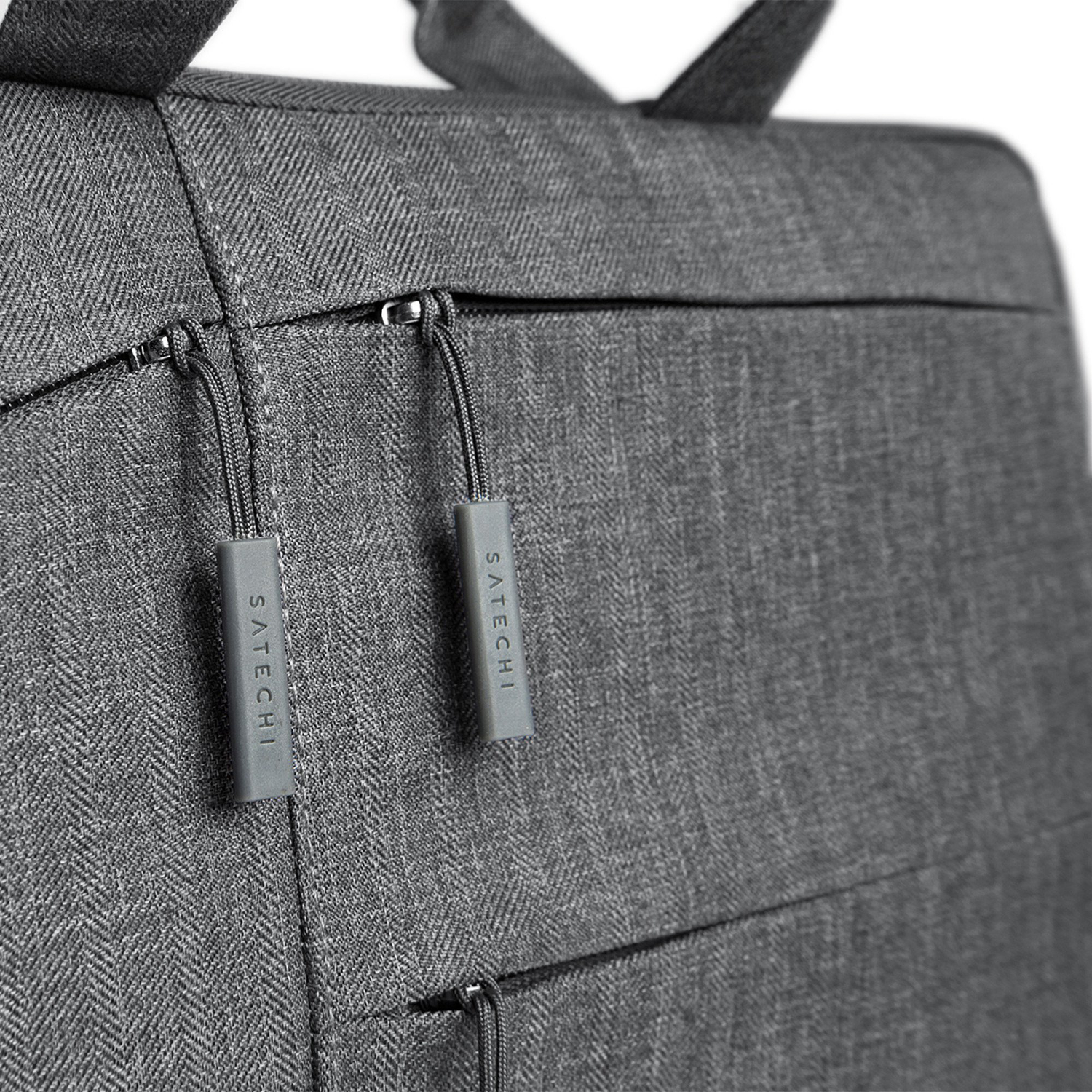 Primo piano di uno zaino grigio con due tiretti grigi con la scritta 'SATECHI'. Tessuto grigio strutturato.