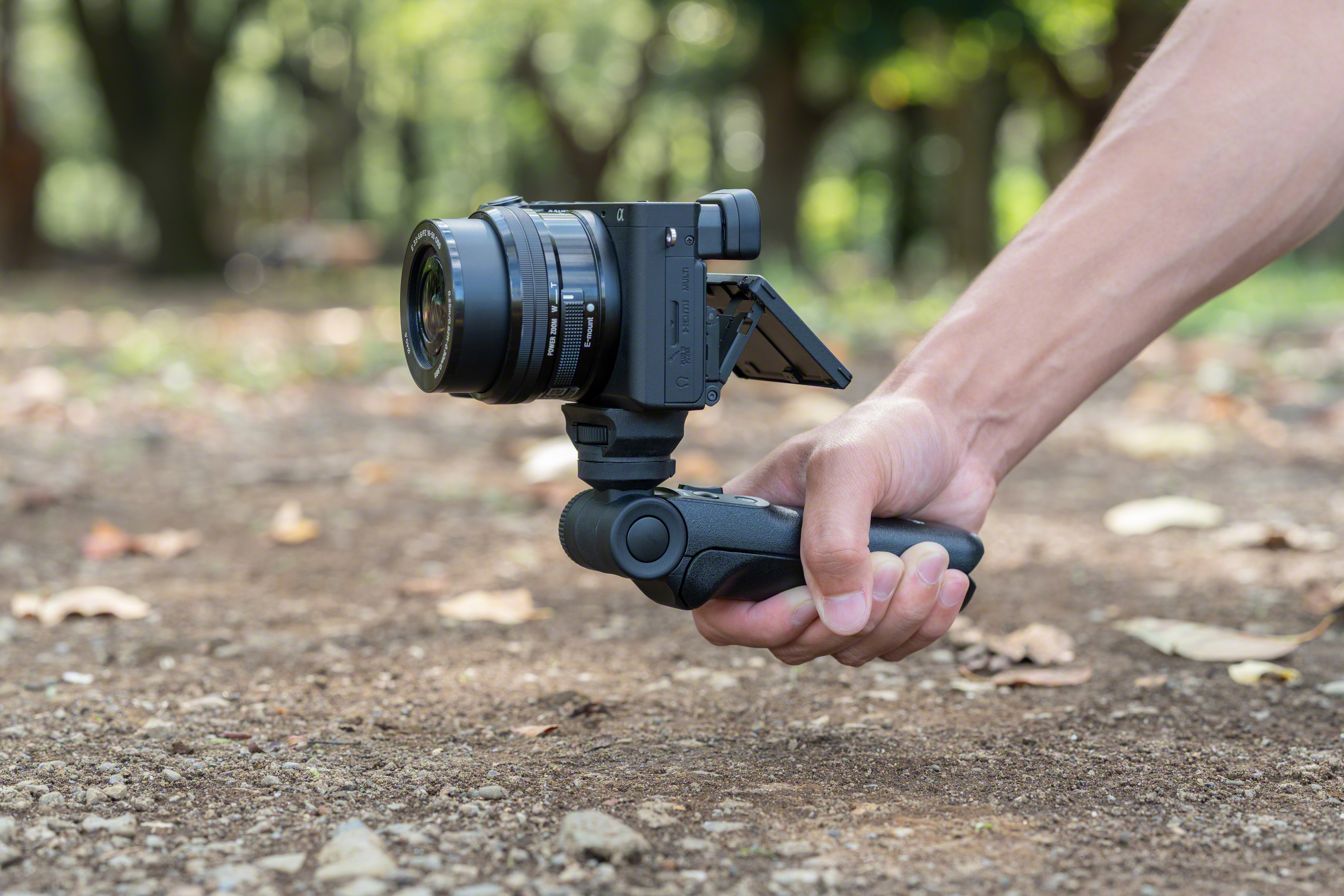 Een persoon die een camera op een gimbal vasthoudt. De camera is zwart en de achtergrond is wazig.
