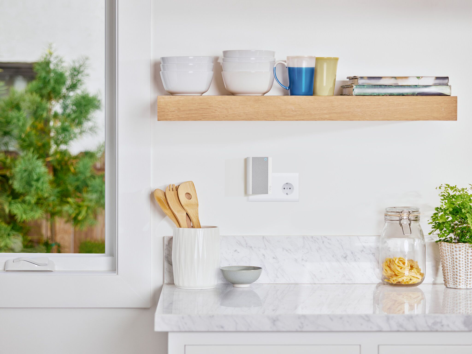 Keukeninterieur met een plank, kommen en een smart home-apparaat. Houten plank, witte muur.