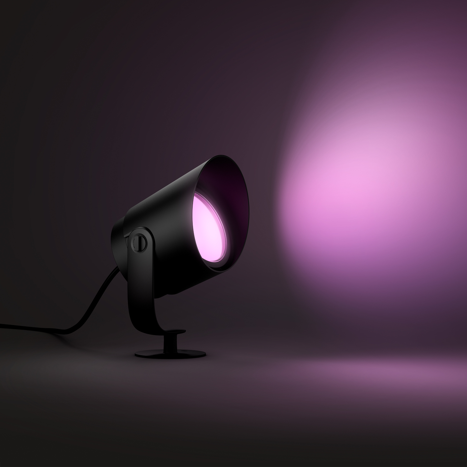 Projecteur Philips Hue noir éclairant une lumière rose sur fond sombre.