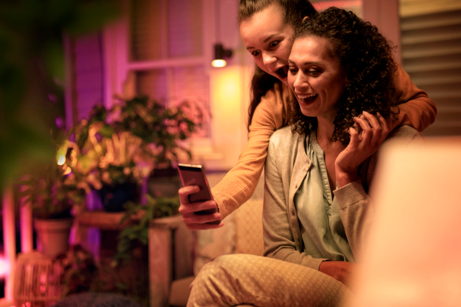 A woman and a girl are looking at a phone with joy. They are outside, with colorful lights.