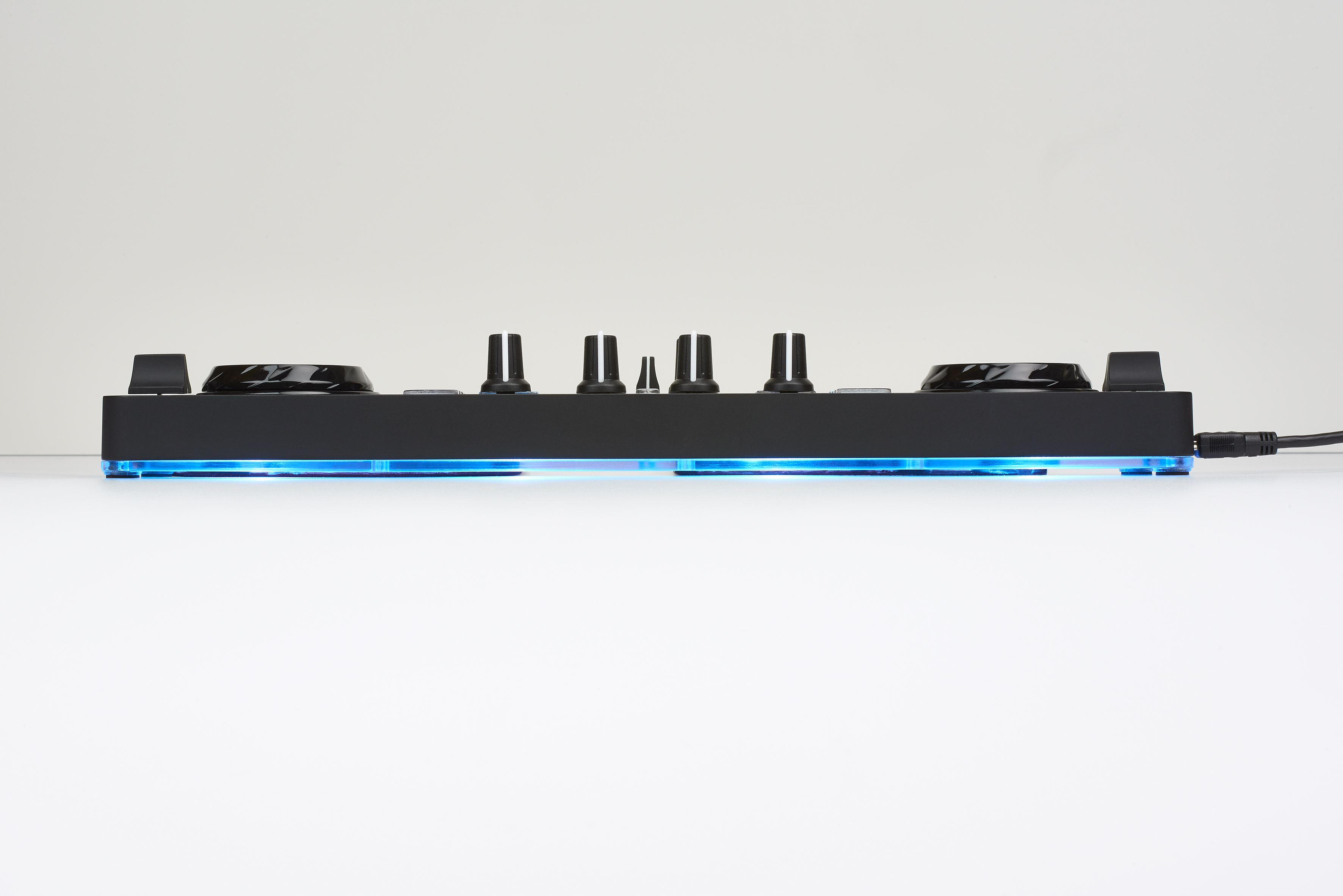 Ein schwarzer DJ-Controller mit mehreren Knöpfen und Tasten. Er steht auf einer weißen Oberfläche.