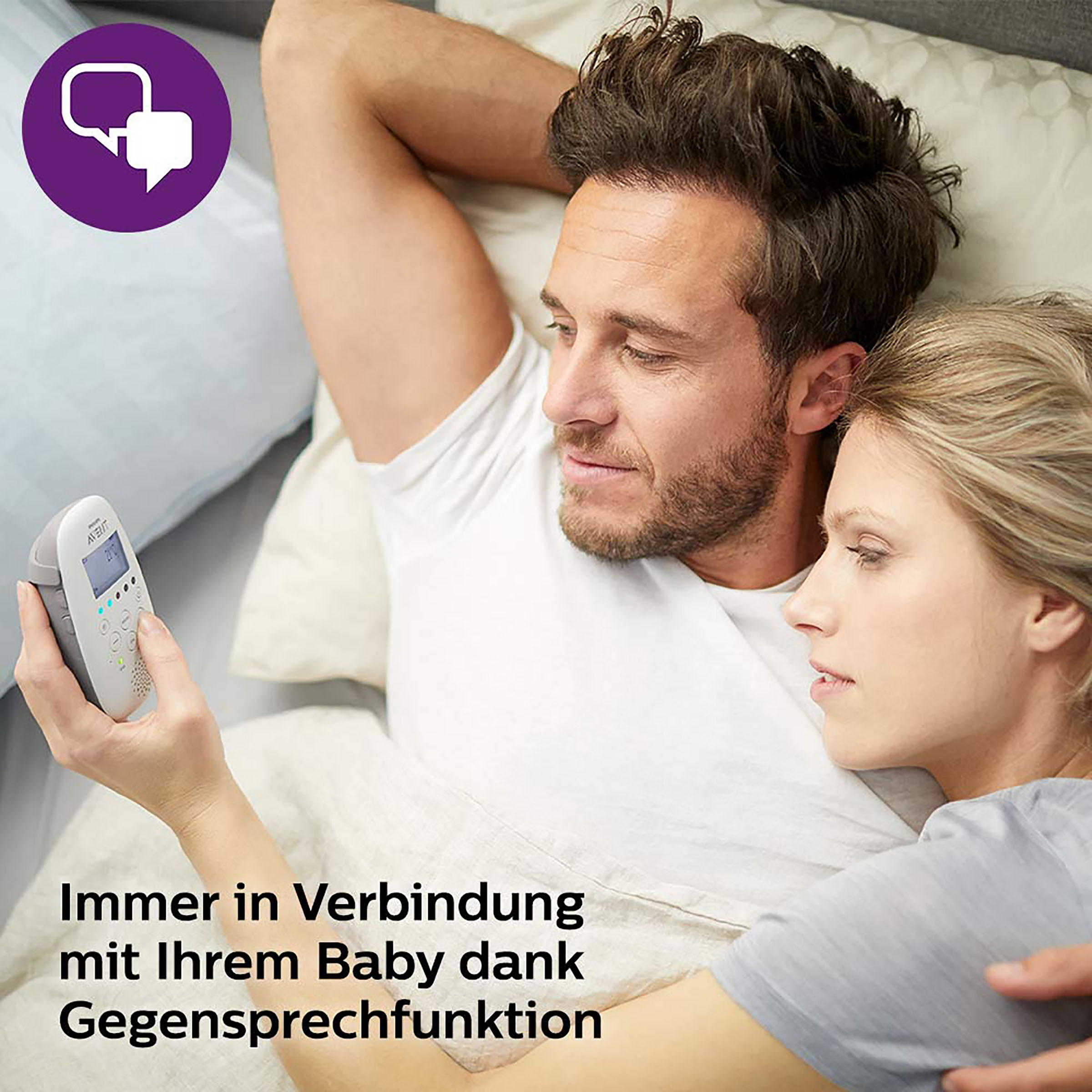 Paar im Bett, das einen Babyphone betrachtet. Text: Immer verbunden.