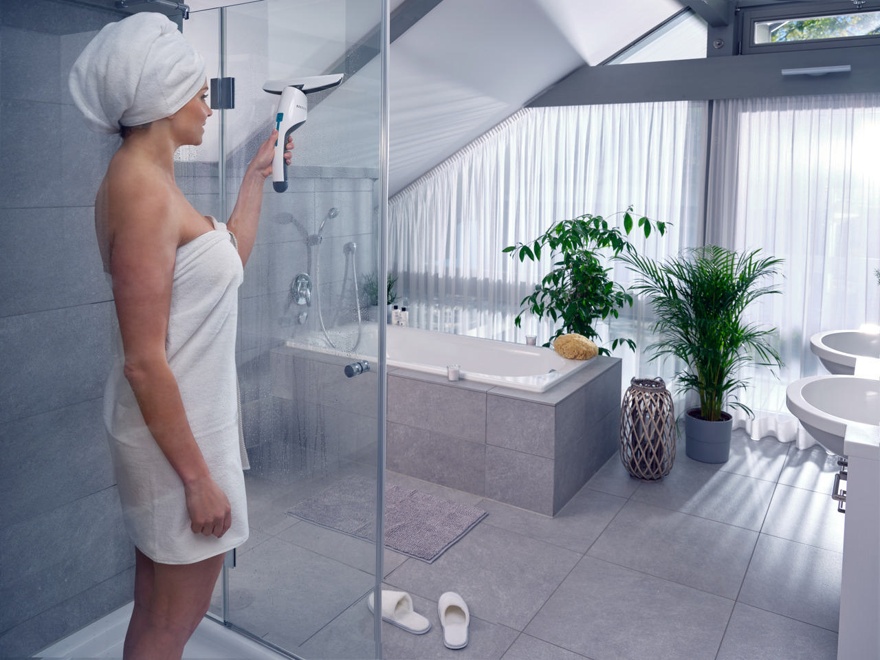 Frau in einem Badezimmer, die eine Duschglasscheibe mit einem Abzieher reinigt, modernes Design.