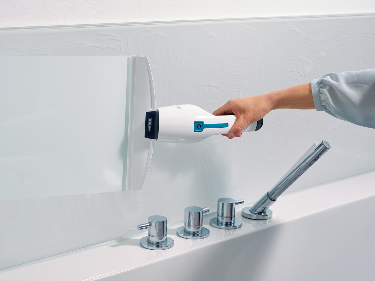 Eine Person reinigt eine weiße Oberfläche mit einem handgehaltenen Reinigungswerkzeug in der Nähe eines Wasserhahns.
