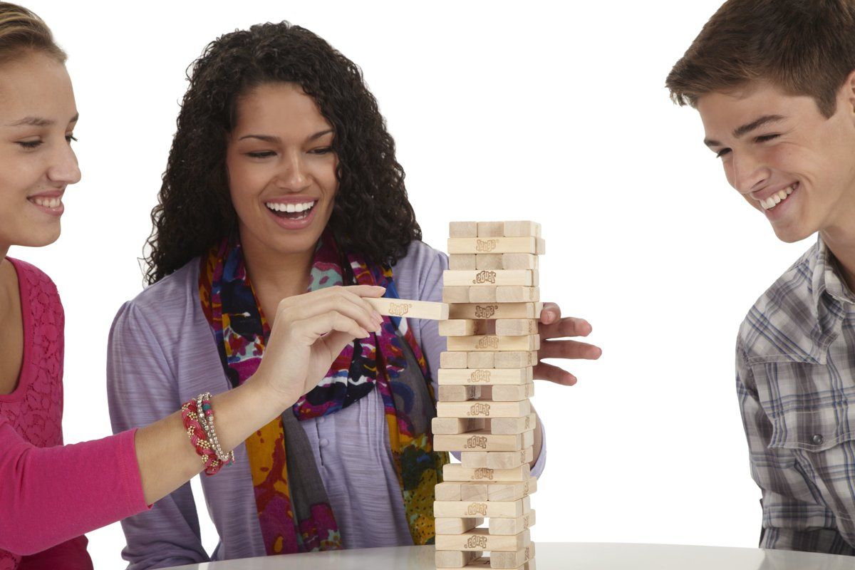 Three people playing Jenga. One is removing a block from the tower. All are smiling.