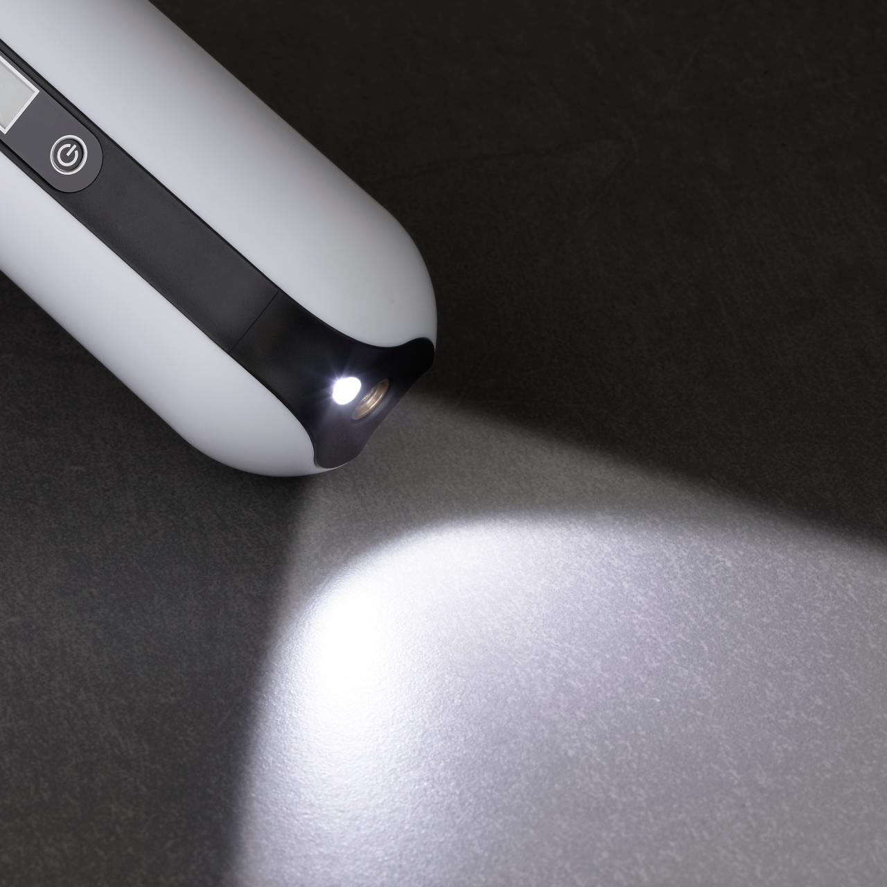 Weiße Taschenlampe, die Licht auf eine dunkle Oberfläche scheint. Fokus auf Lichtquelle.