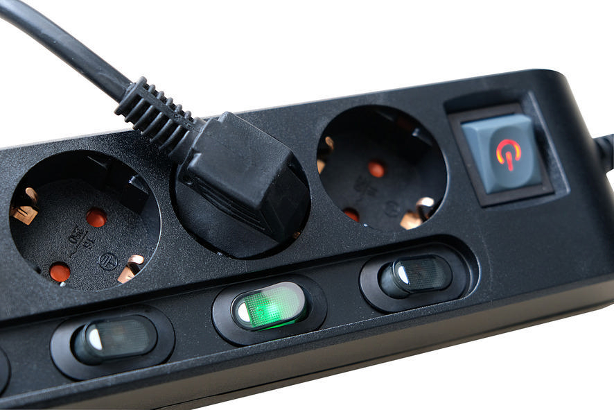 Schwarze Steckdosenleiste mit eingestecktem Stecker. Grünes Licht an.