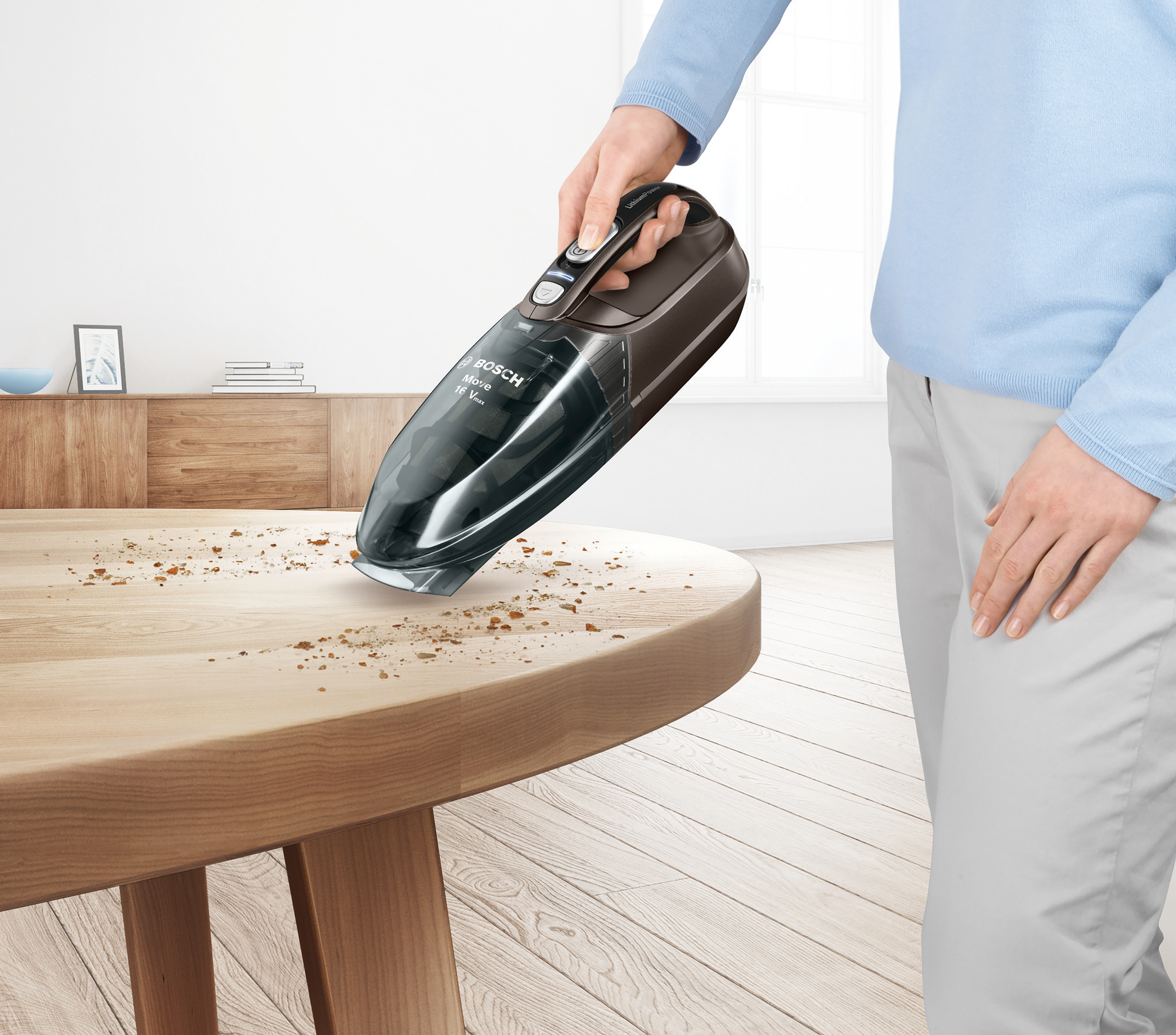 Eine Person benutzt einen Bosch-Staubsauger auf einem Holztisch. Krümel sind sichtbar.