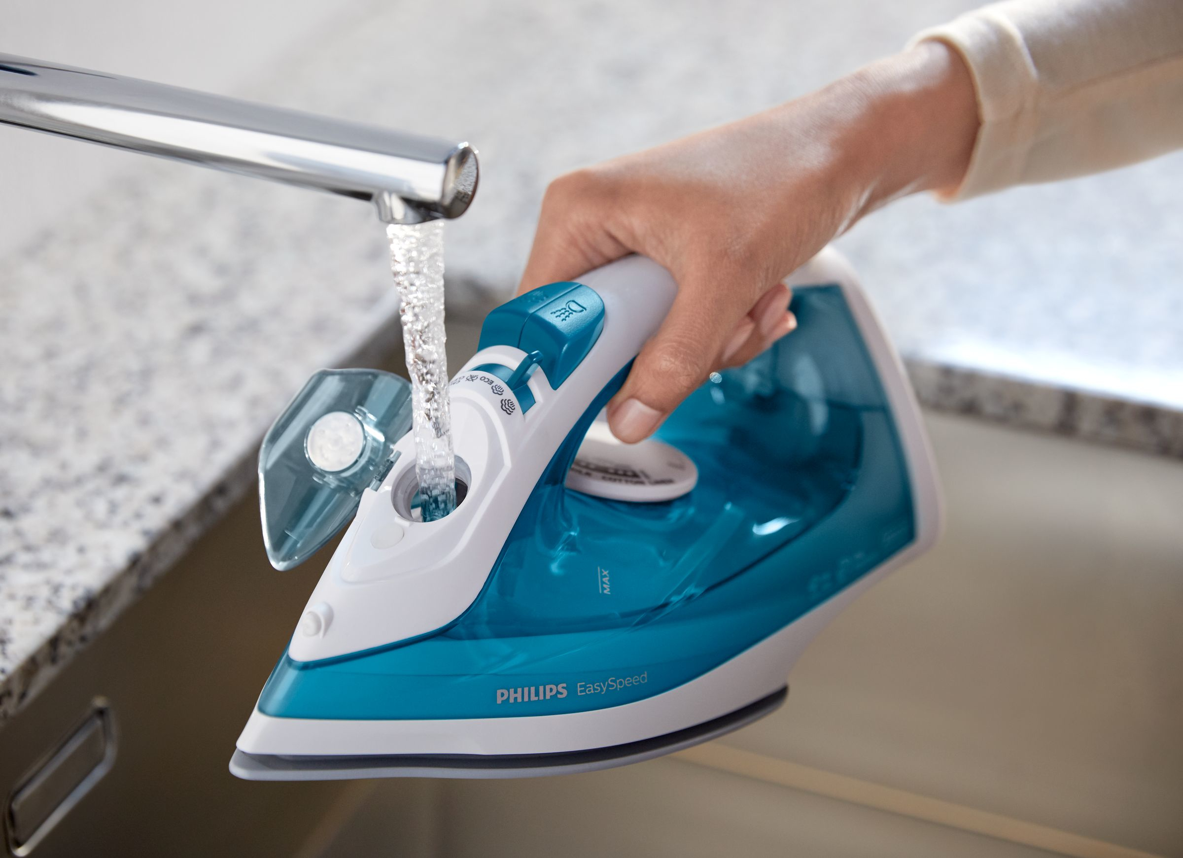 Mano che riempie ferro da stiro blu e bianco con acqua dal rubinetto.