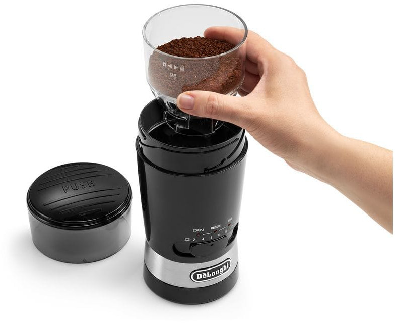 Black and silver coffee grinder with ground coffee. Hand pouring coffee grounds into the grinder.