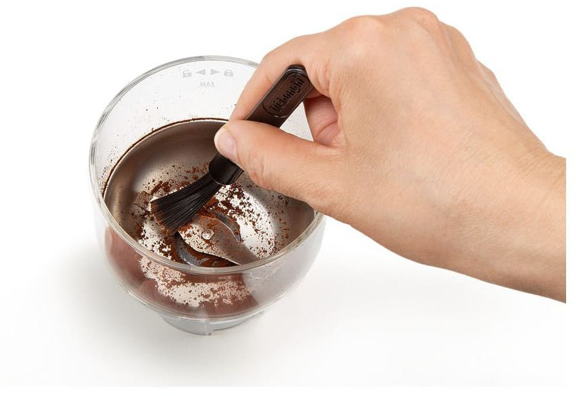 Hand holding a brush, cleaning the inside of a coffee grinder with coffee grounds.