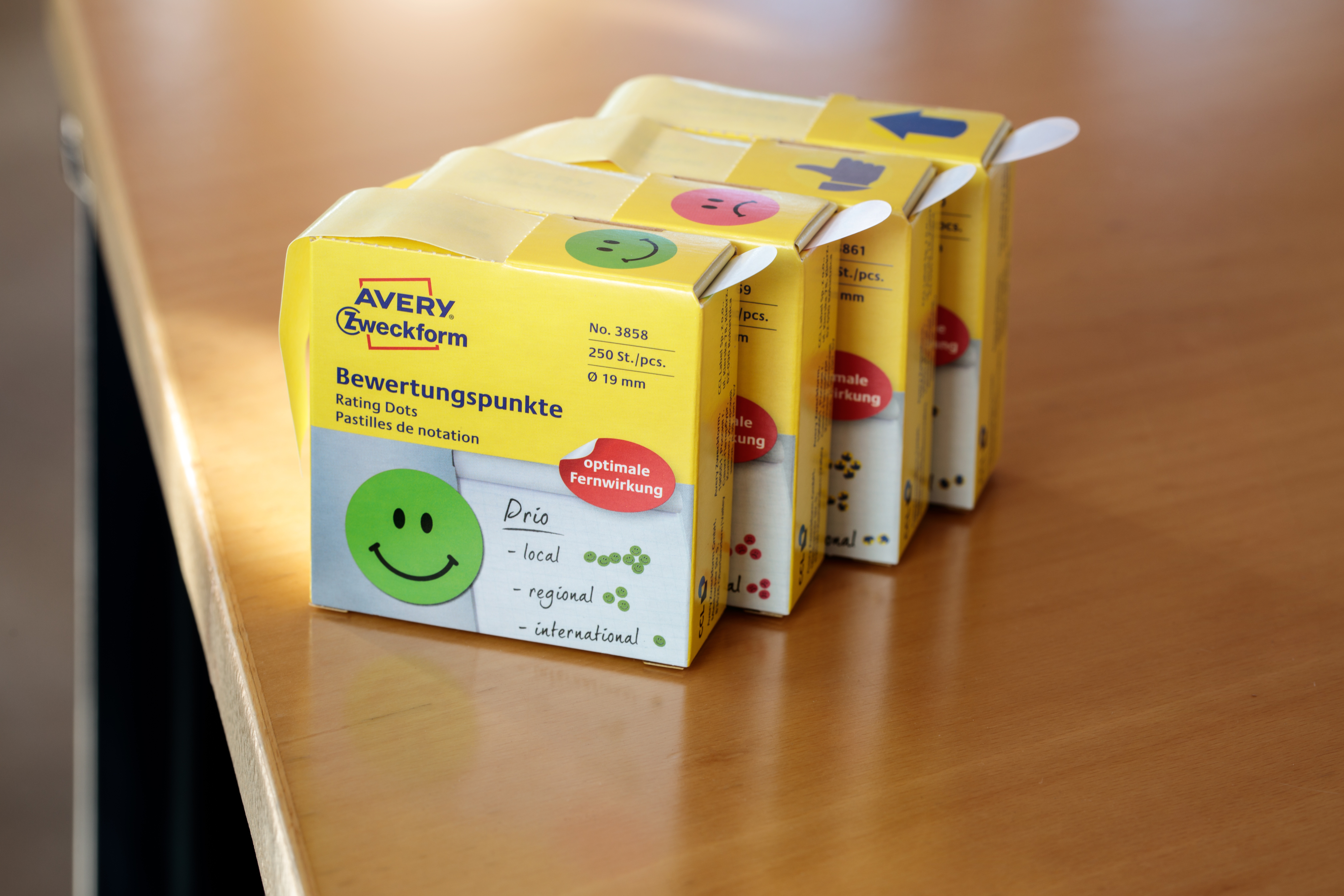 Vier gelbe Schachteln mit Bewertungs-Punkten auf einem Holztisch. Jede Schachtel hat einen anderen Smiley.